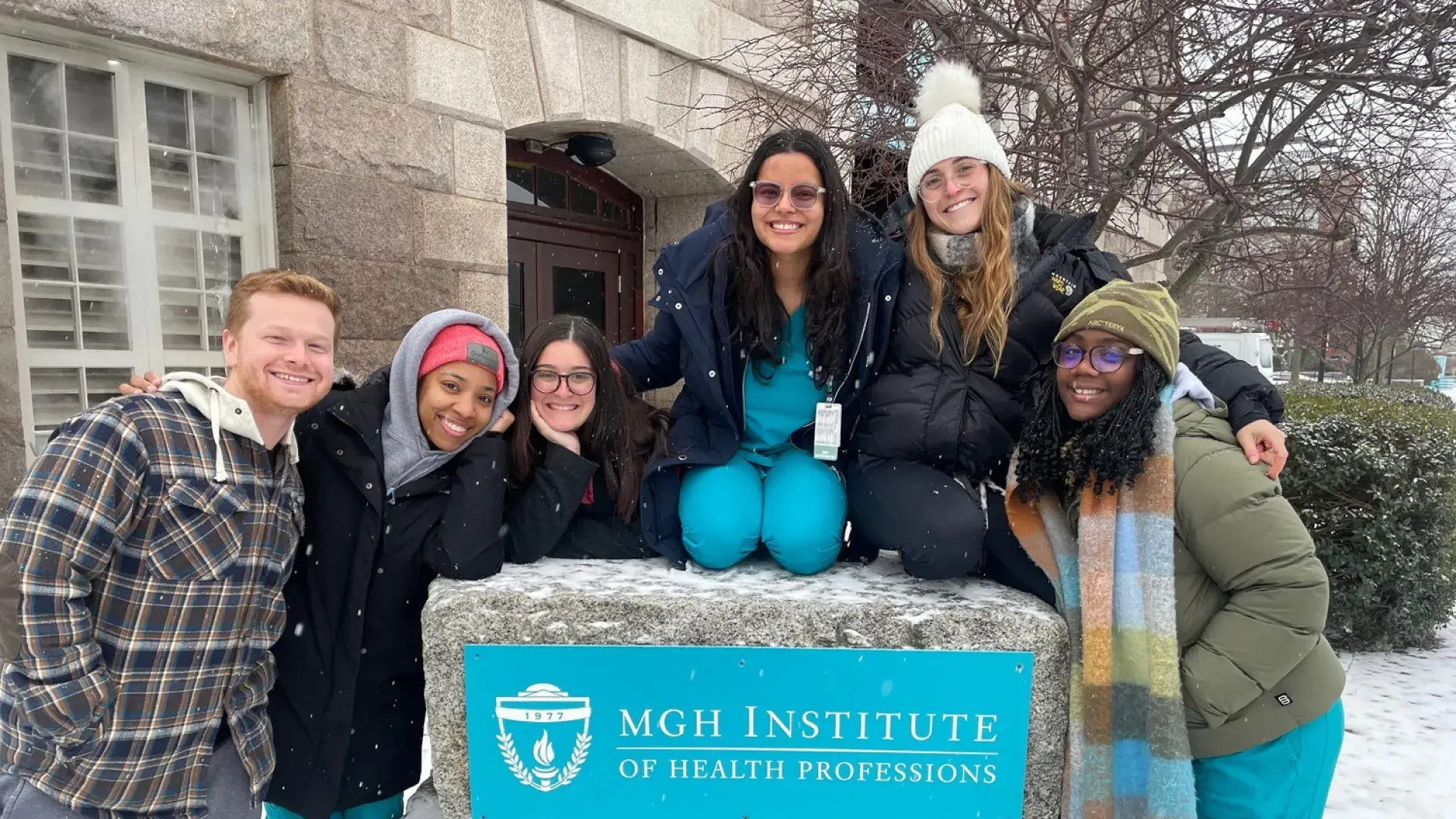 students in scrubs gather around the IHP sign on campus