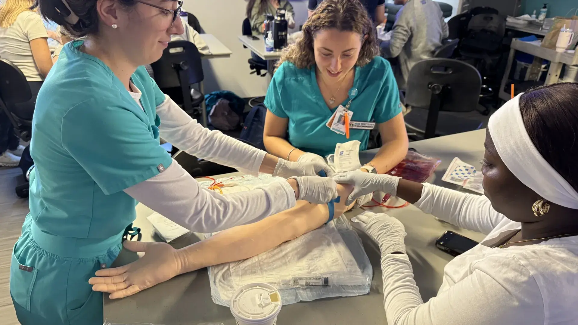 3 women giving IV to fake arm