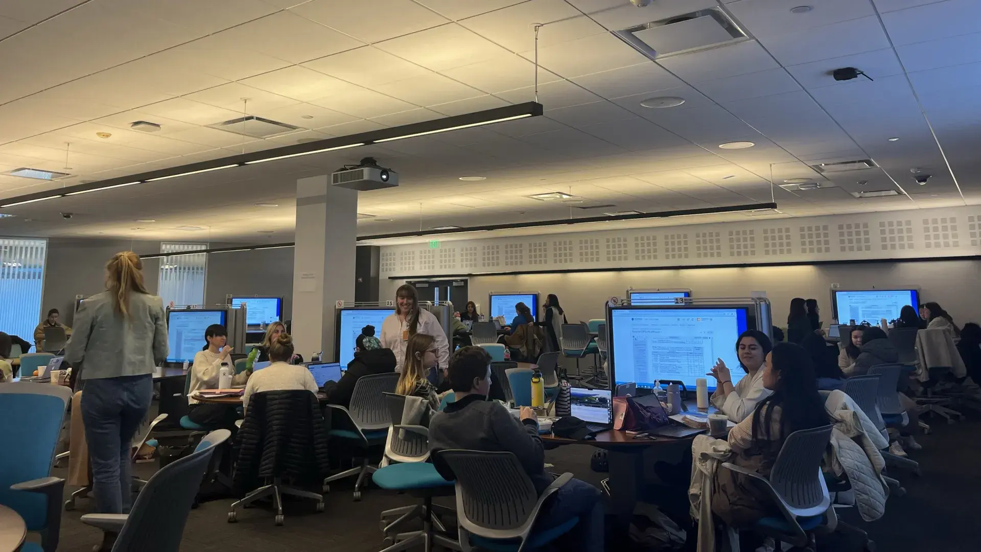 A room with tables that have large monitors with people sitting 
