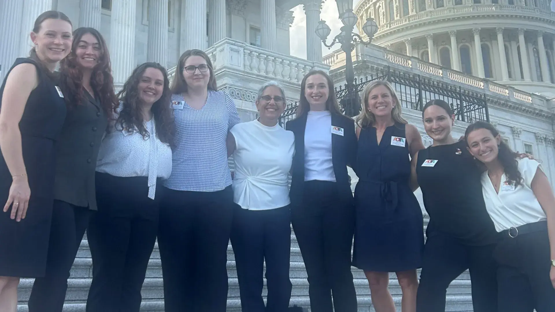 Nine people stand on steps with the US Capitol in the background