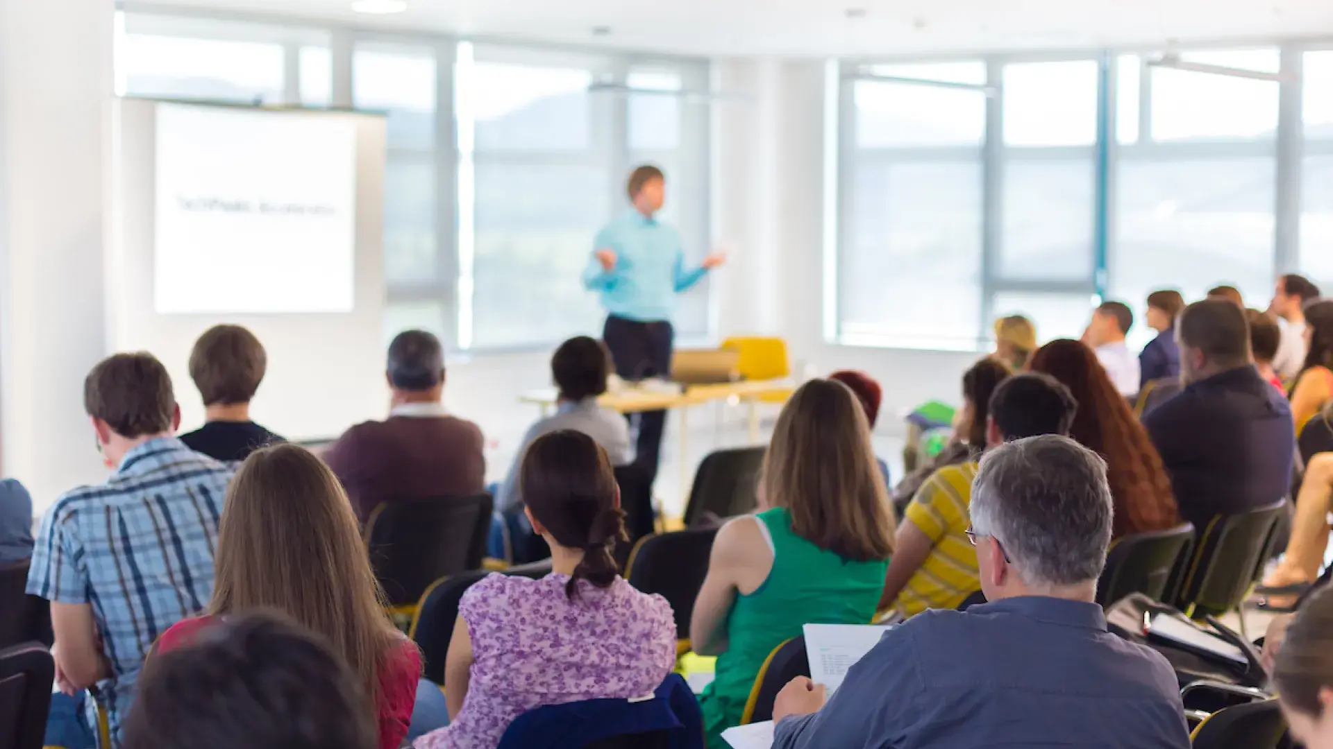 adult students learn from a teacher at the front of a classroom