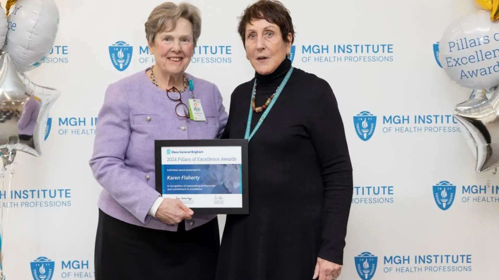 Two women pose in front of a backdrop holding an award