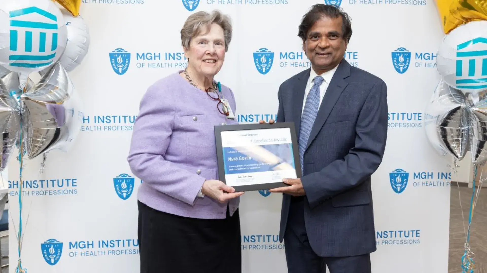 Two people pose in front of a backdrop holding an award