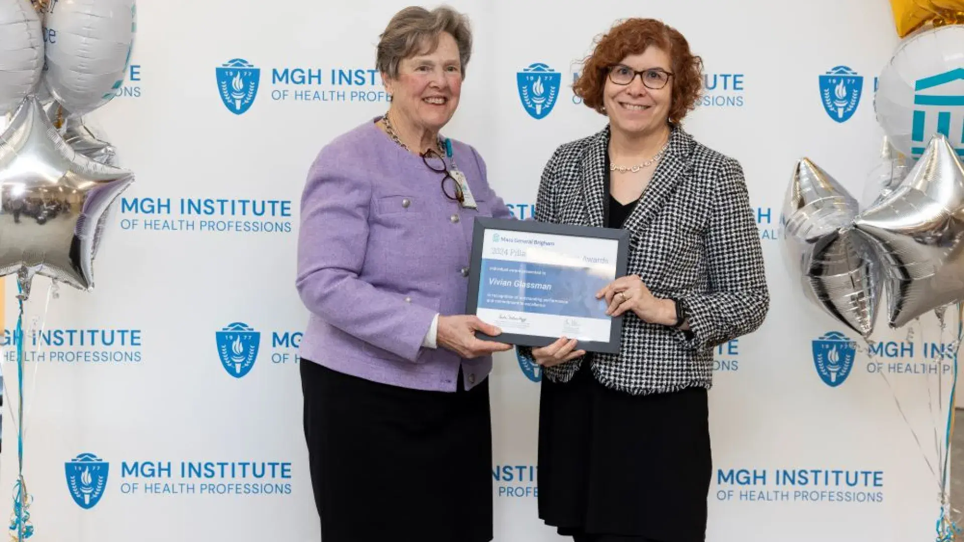 Two women pose in front of a backdrop holding an award
