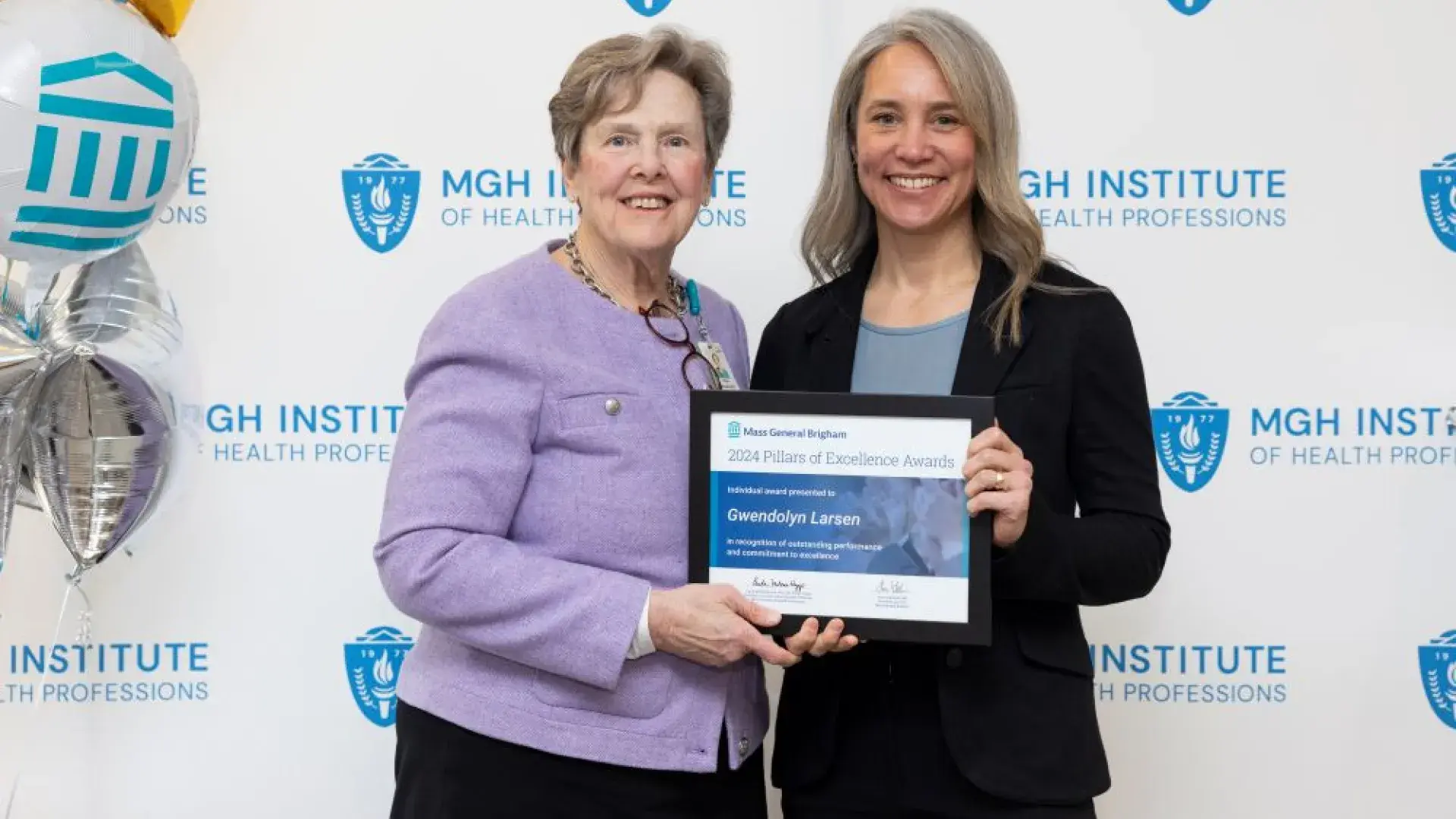 Two people pose in front of a backdrop holding an award