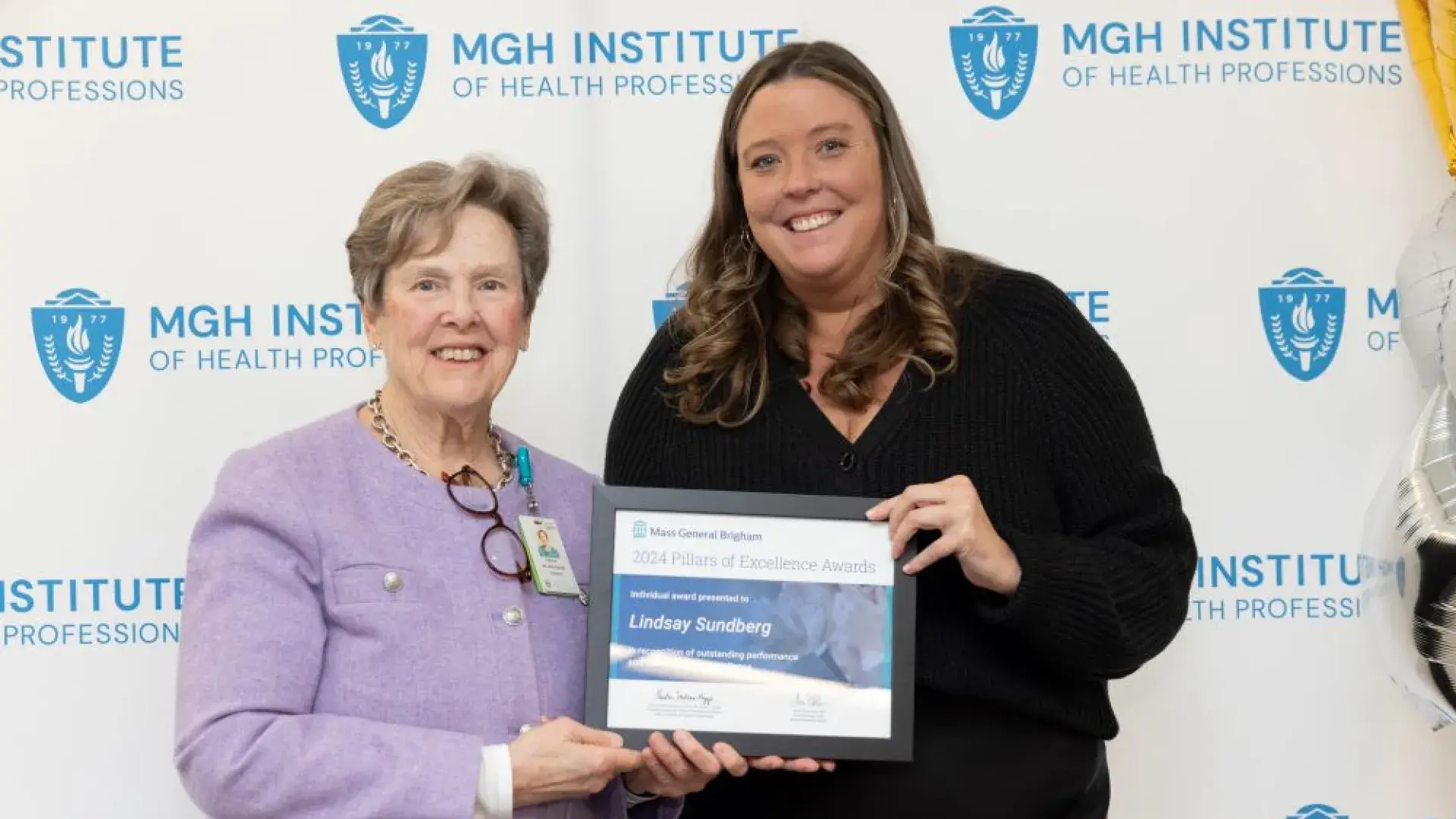 Two women pose in front of a backdrop holding an award