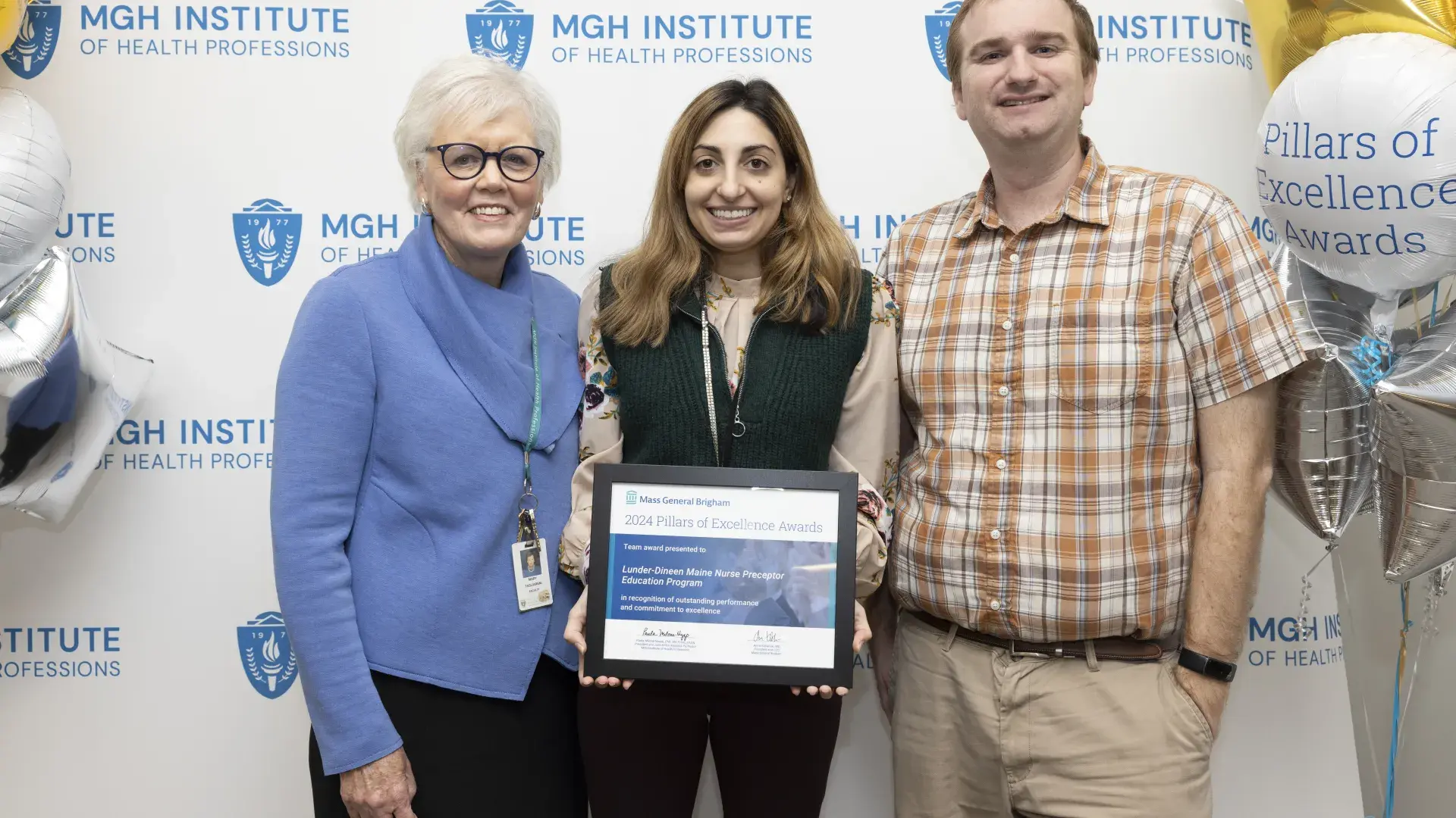 Three people stand in front of a background holding an award