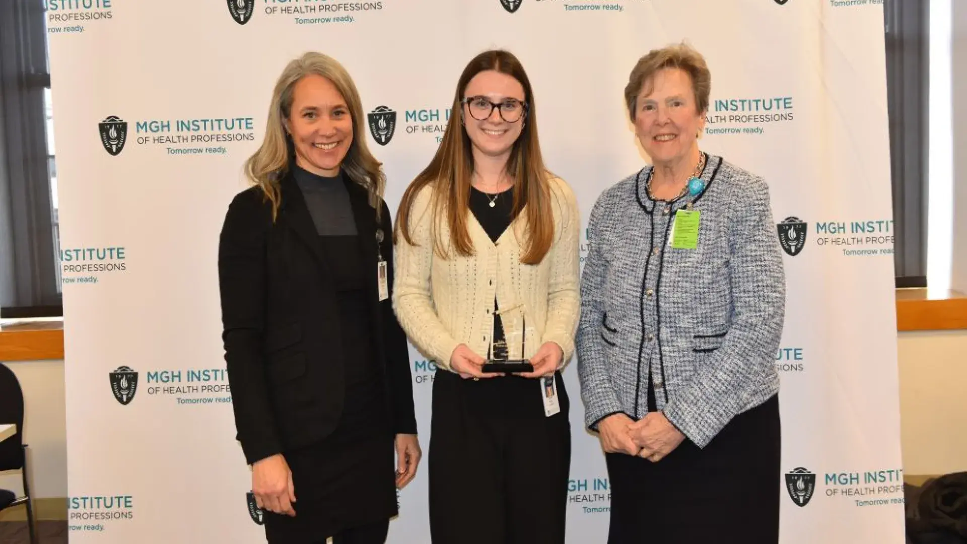 Three people stand in front of a background holding an award