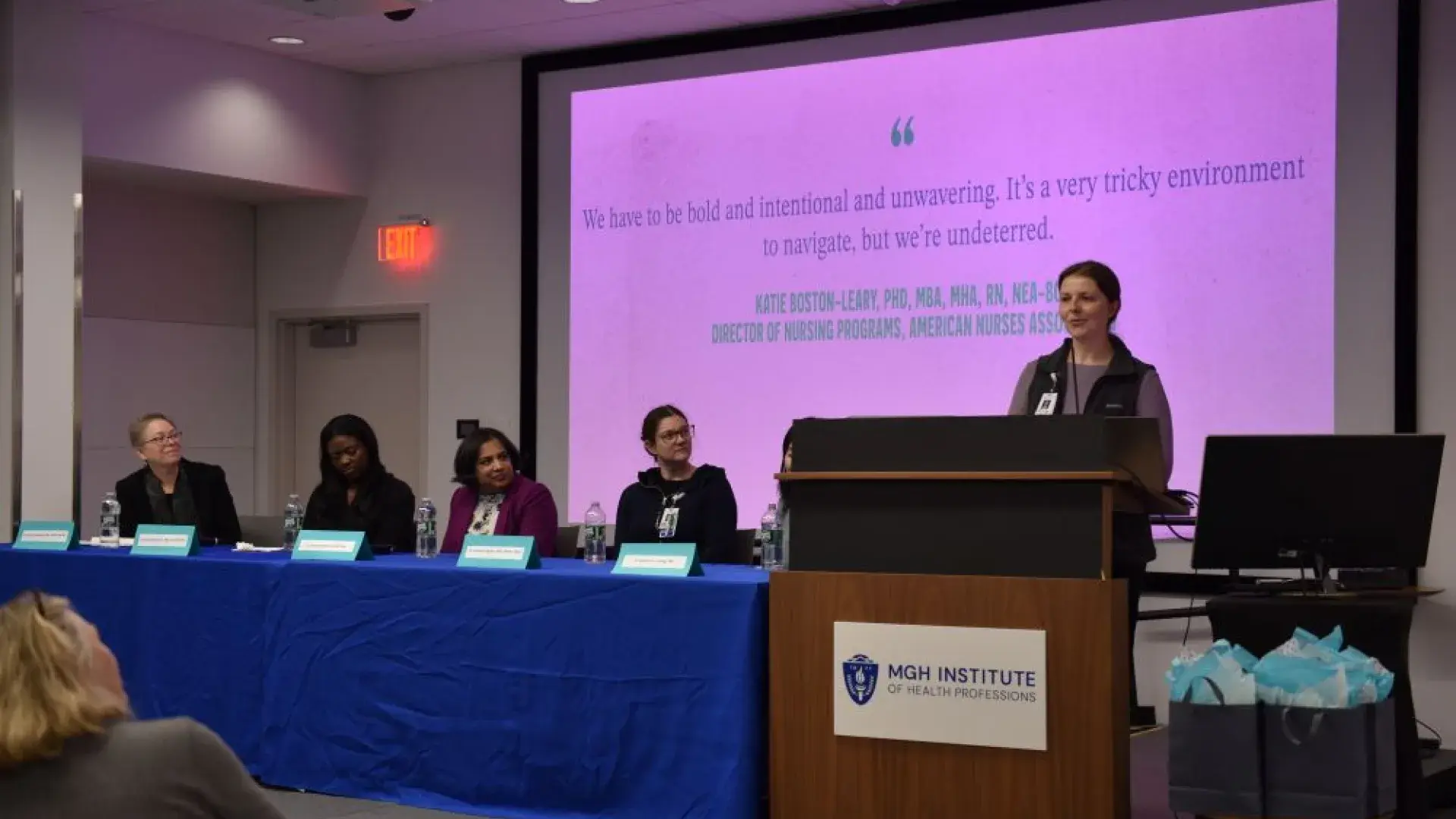 A woman stands at a podium while a panel of people watches her