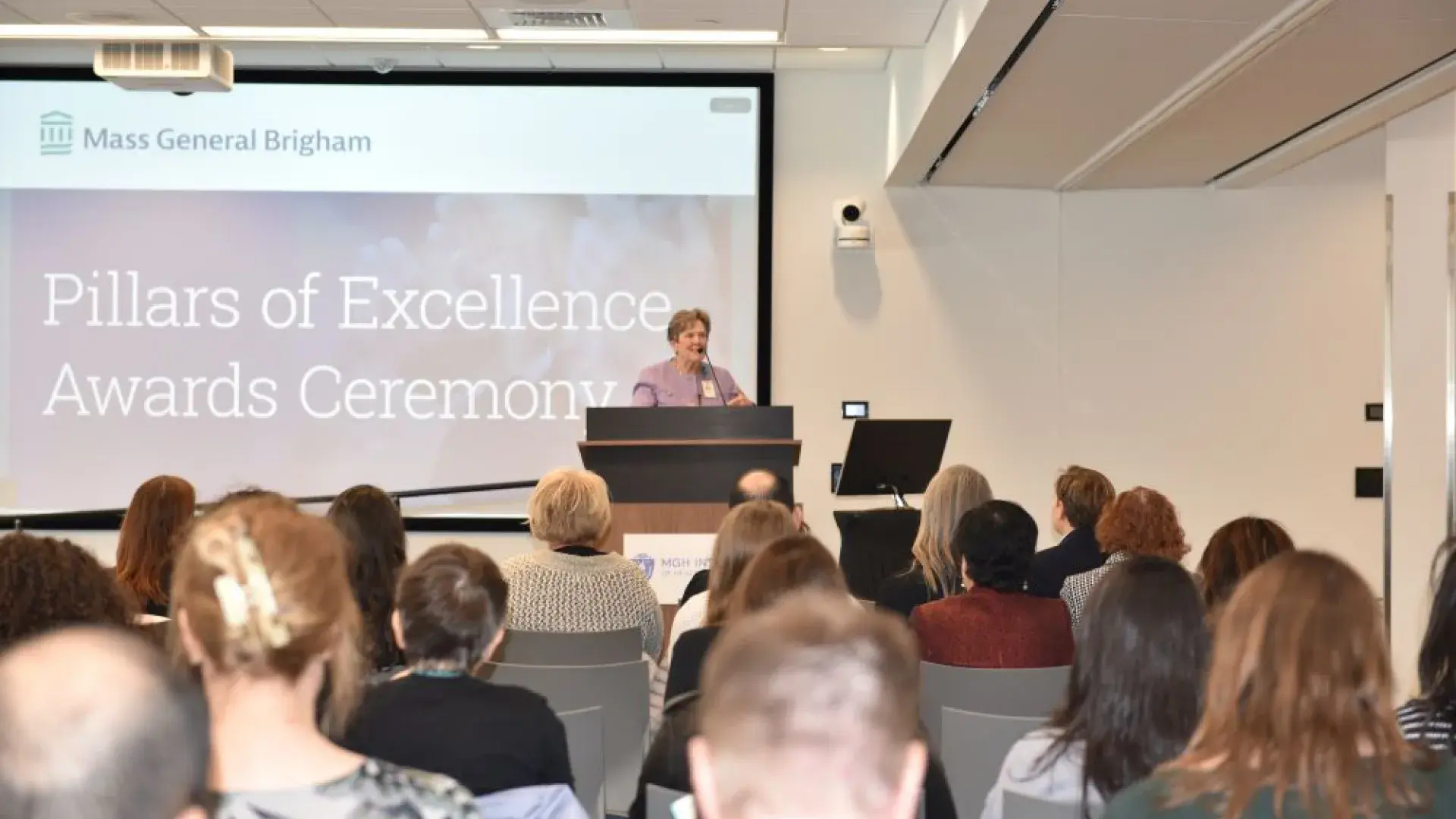 A woman stands at a podium with an audience in the foreground