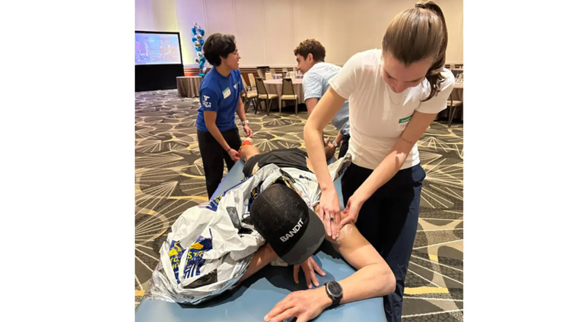 A woman massages the arm of a runner lying on a table while two others work on the legs