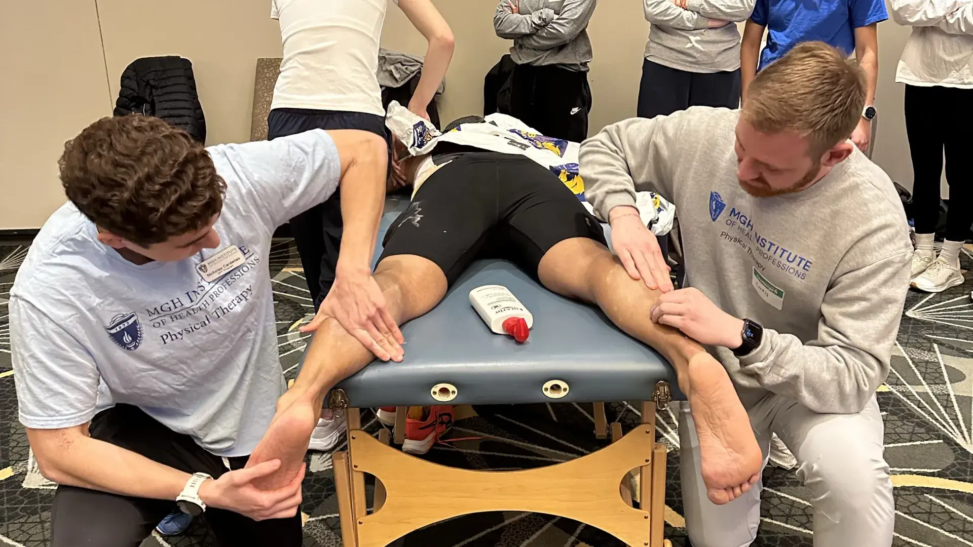 Two people massage the legs of a person on a table