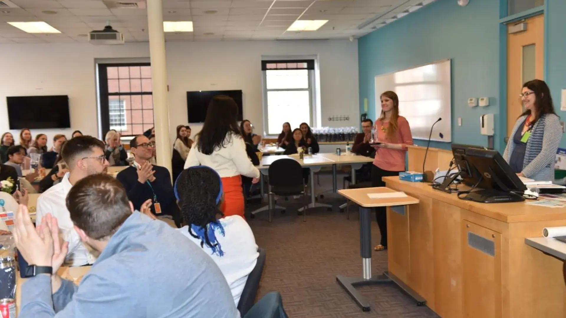People sitting at tables watch a person go to accept an award