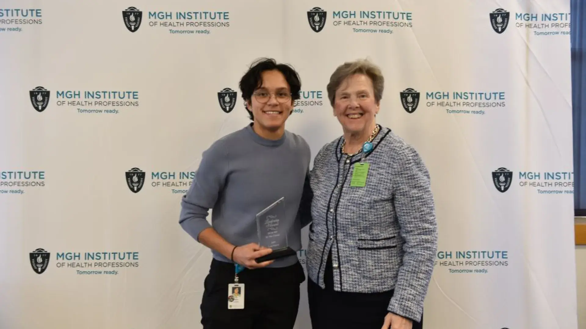 Two women pose in front of a backdrop holding an award