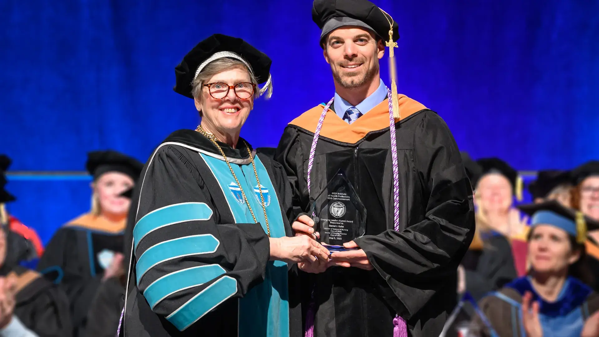 two people in graduation robes hold a crystal award