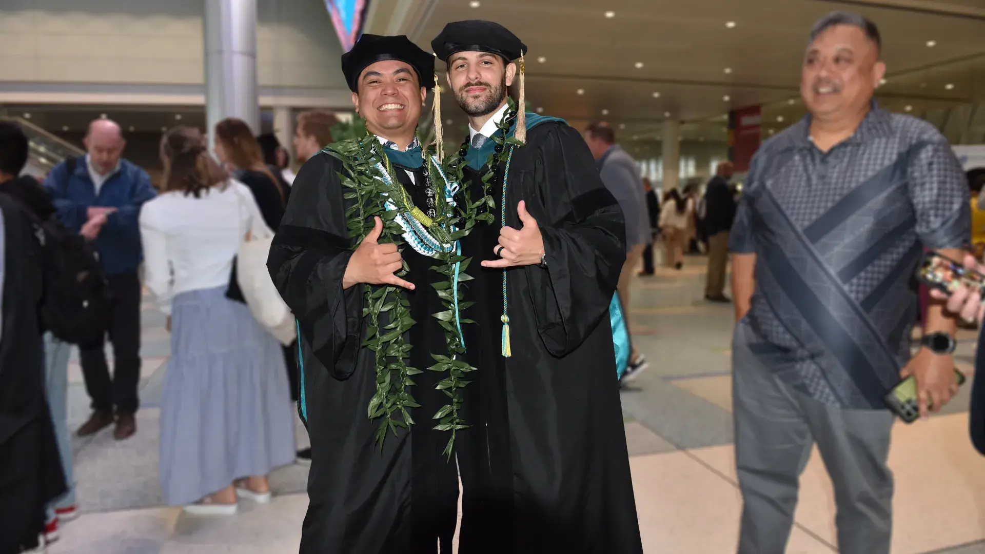 Two men pose wearing graduation robes