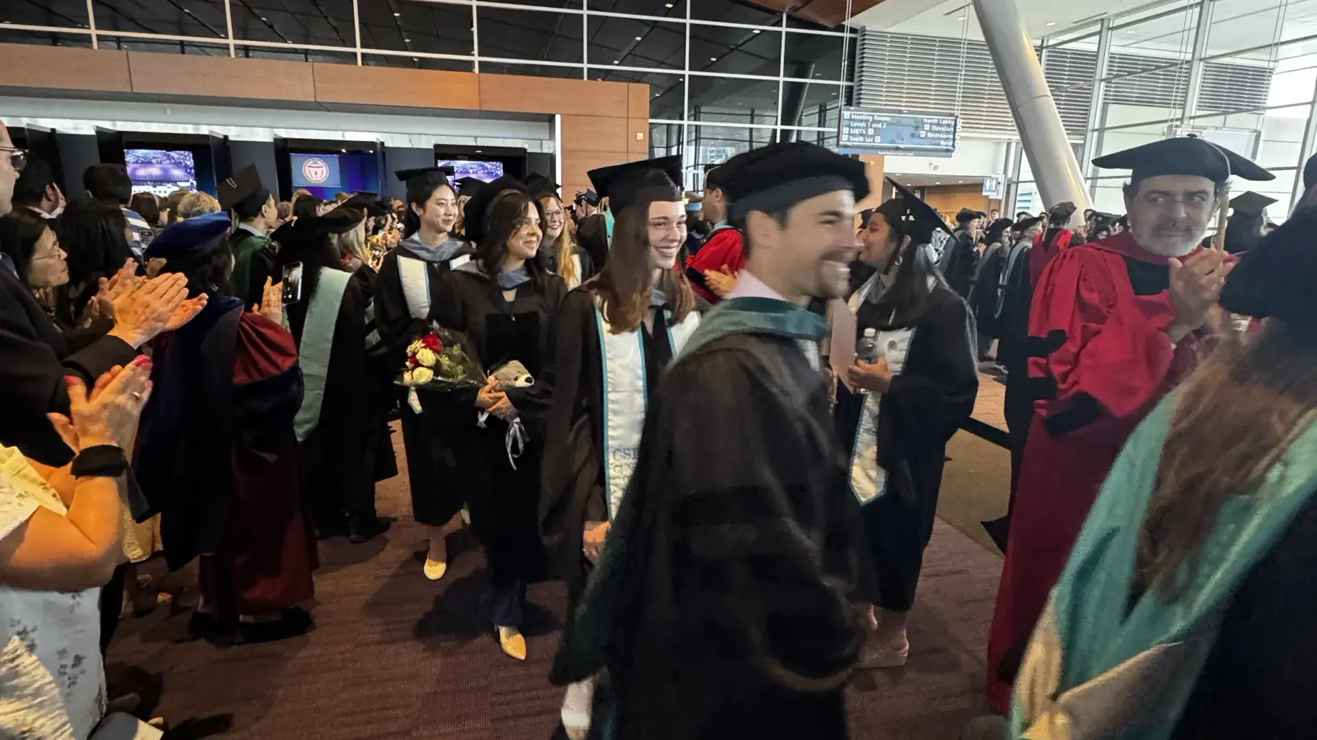 Group of people in cap and gowns walking through several people. 