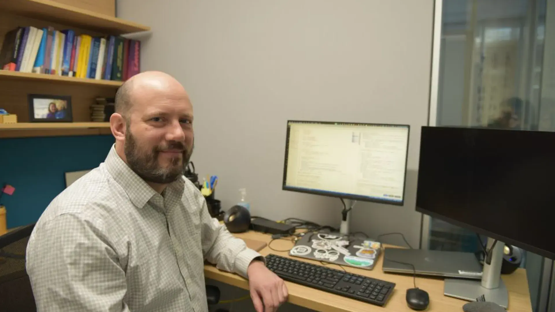 A man sits at a desk with a computer monitor behind him