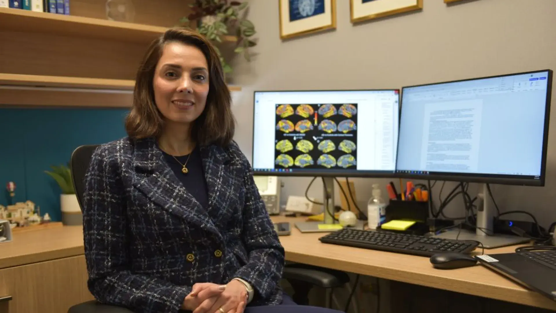 A women faces the camera while sitting at a desk with computer screens behind her