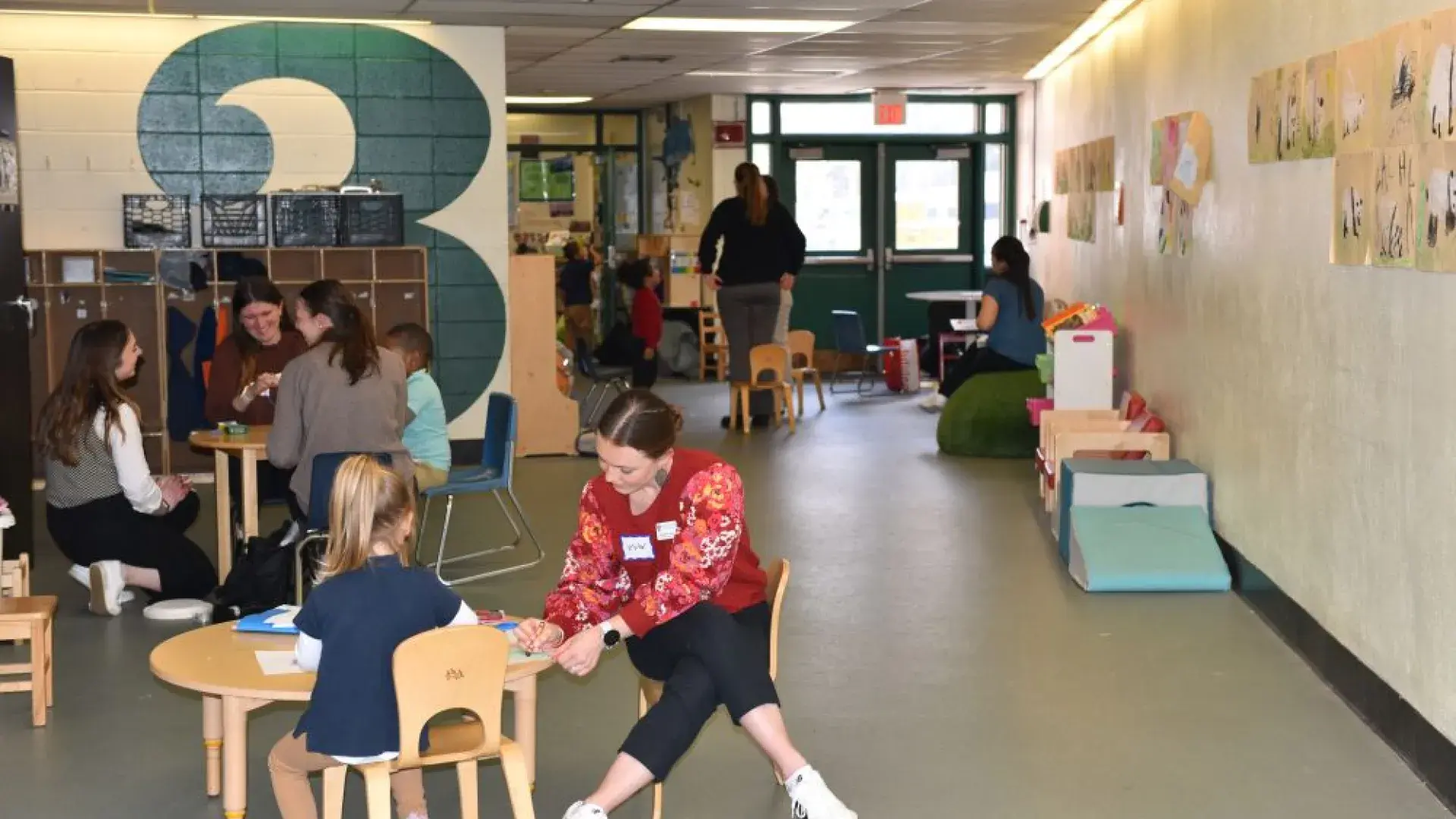 A woman sits at a small table with a child while people in the background do the same