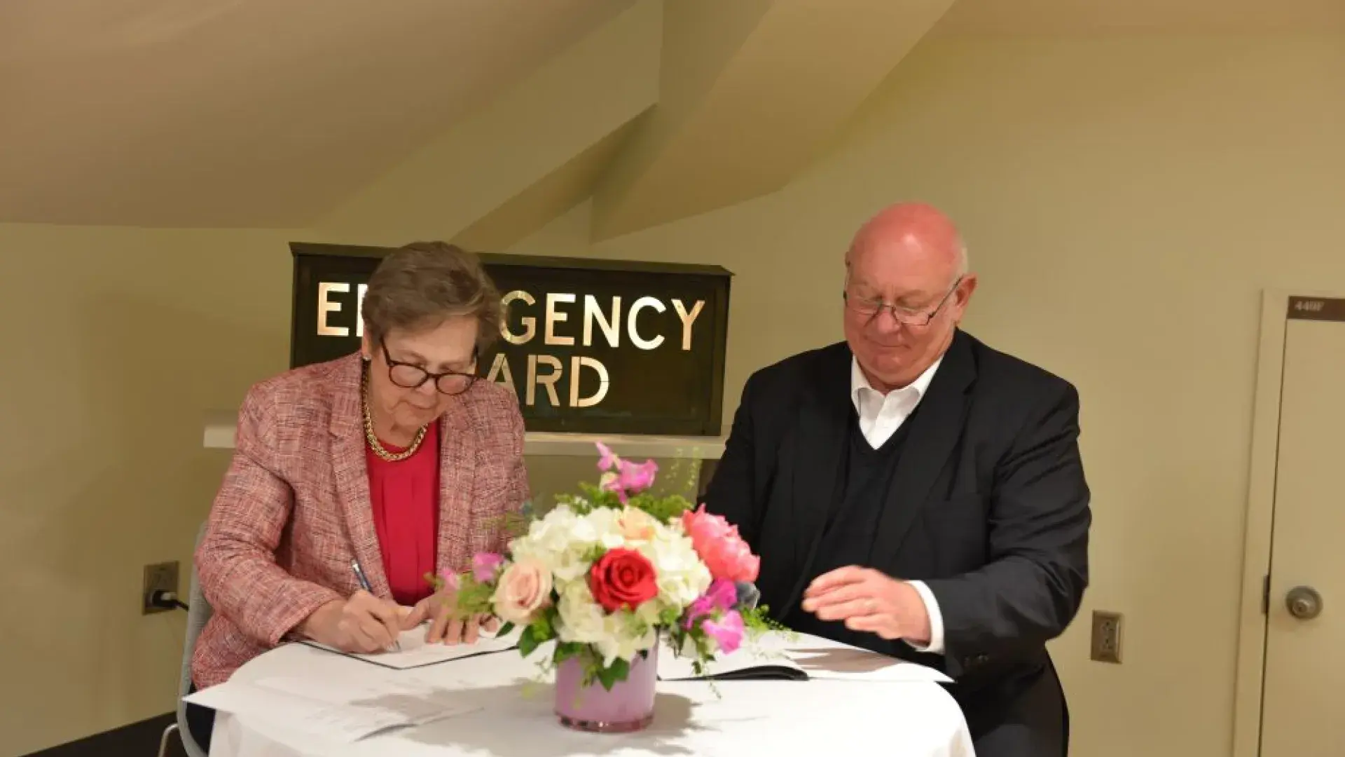 Two people sit next to each other at a table writing on paper