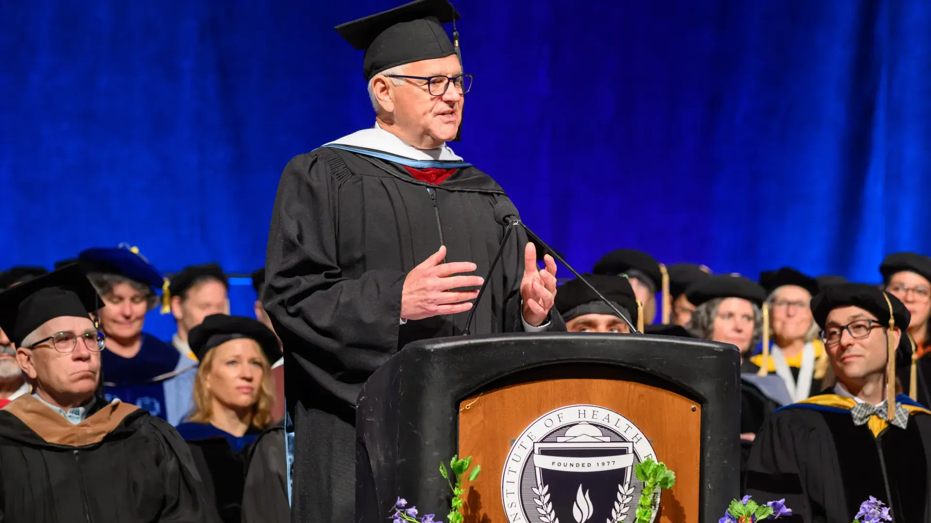 A man wearing a graduation robe stands at a podium