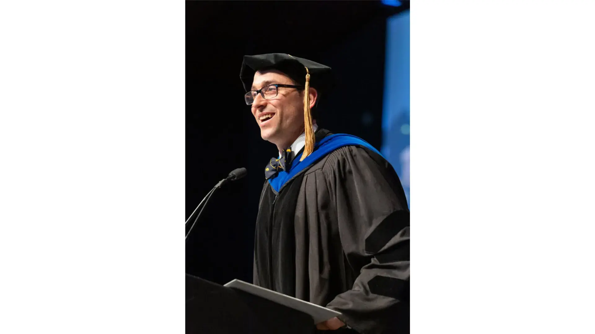 A man wearing a graduation robe stands at a podium