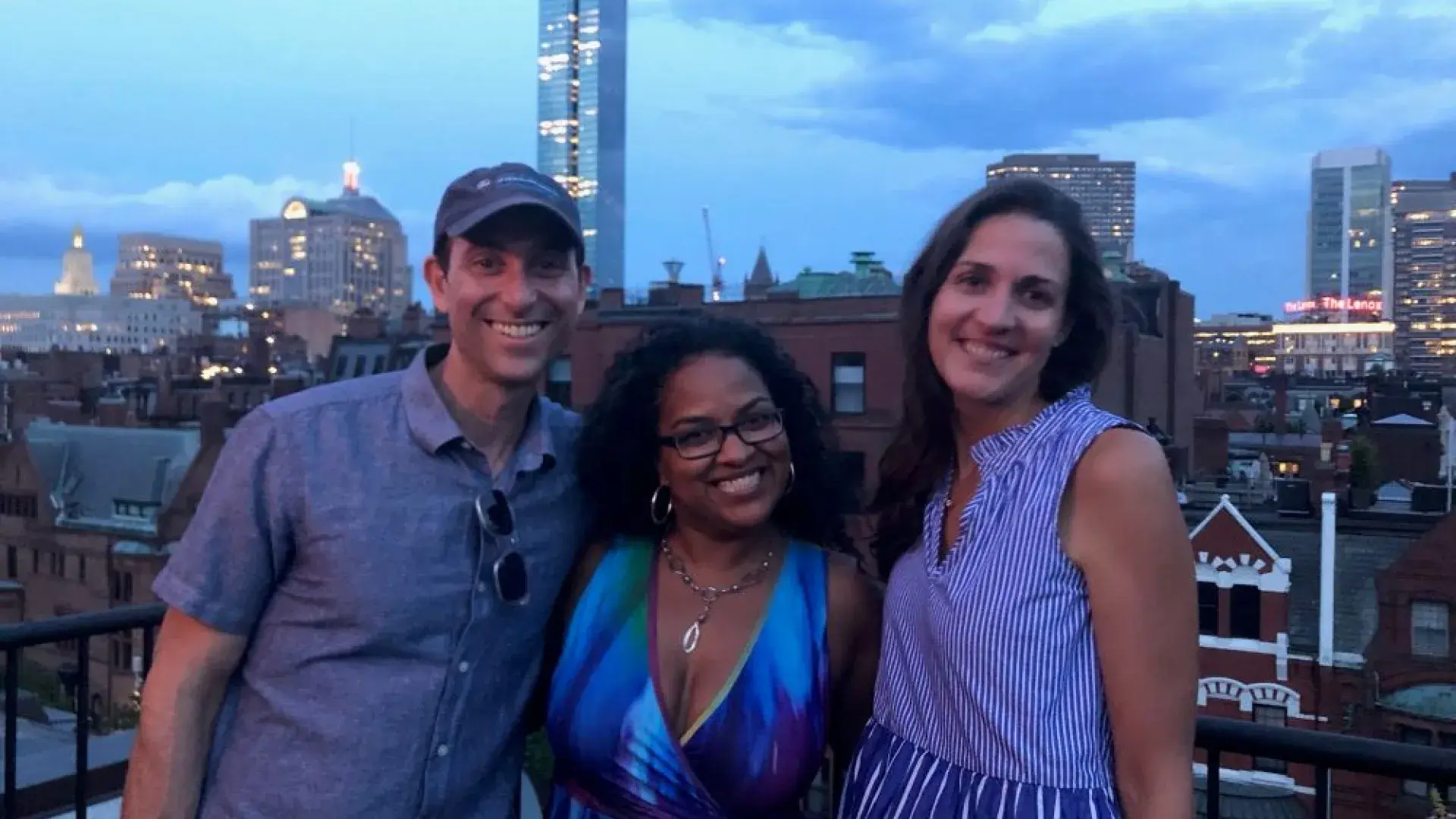 Three people pose for the camera with an urban skyline behind them