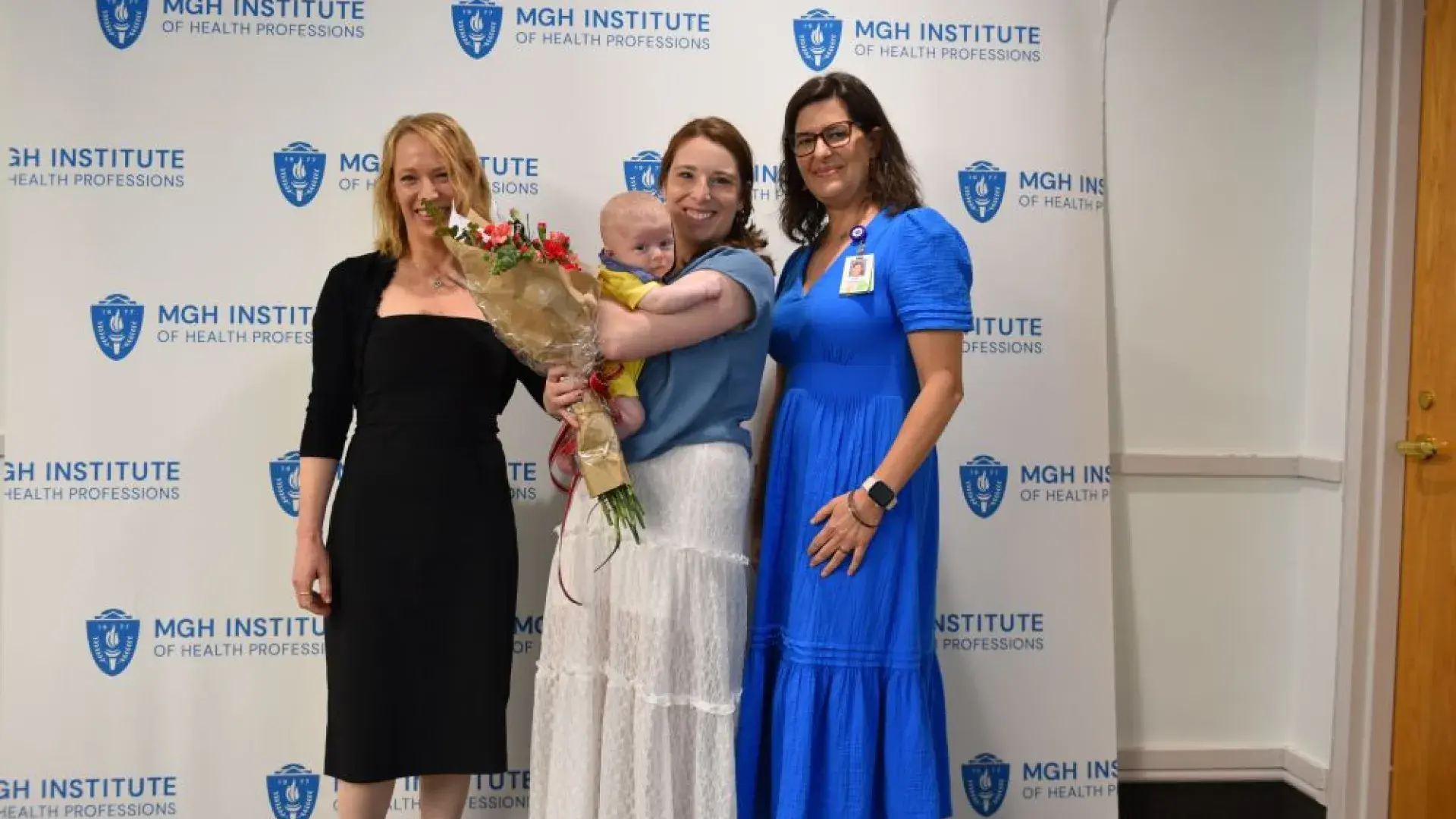 Three people stand in front of a backdrop with one of them holding a baby