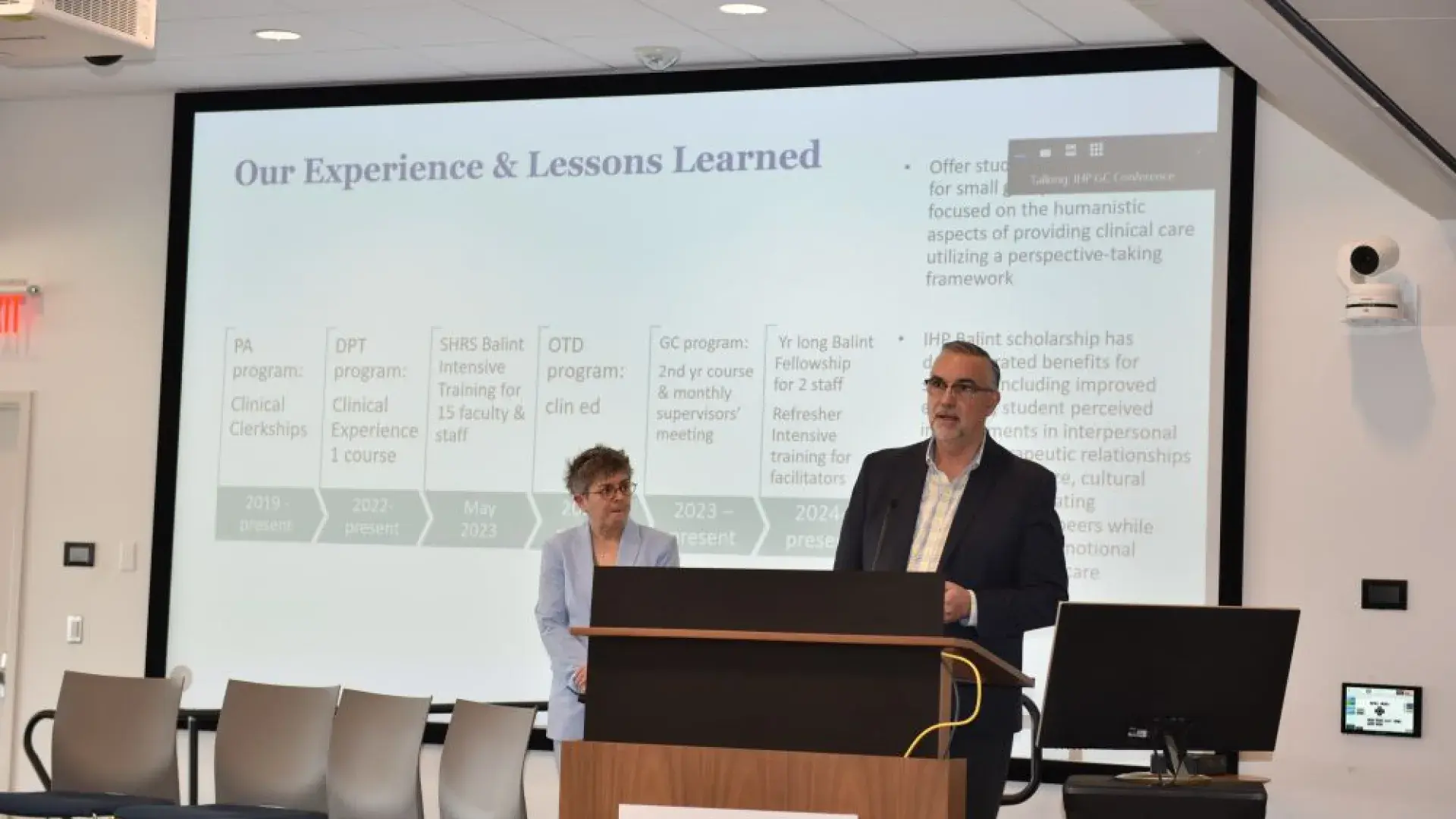 A man stands at the podium while a woman looks on from the stage
