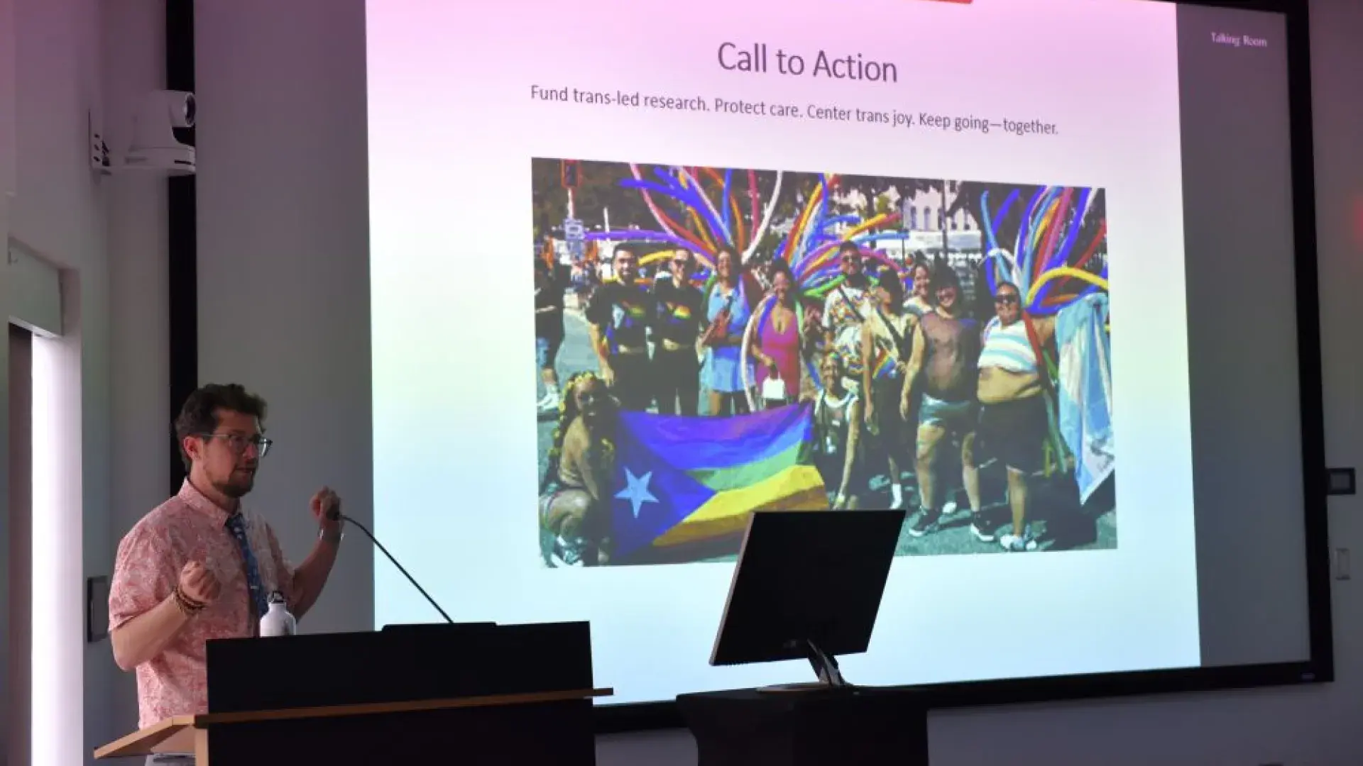 Man standing to left of screen with group photo on it