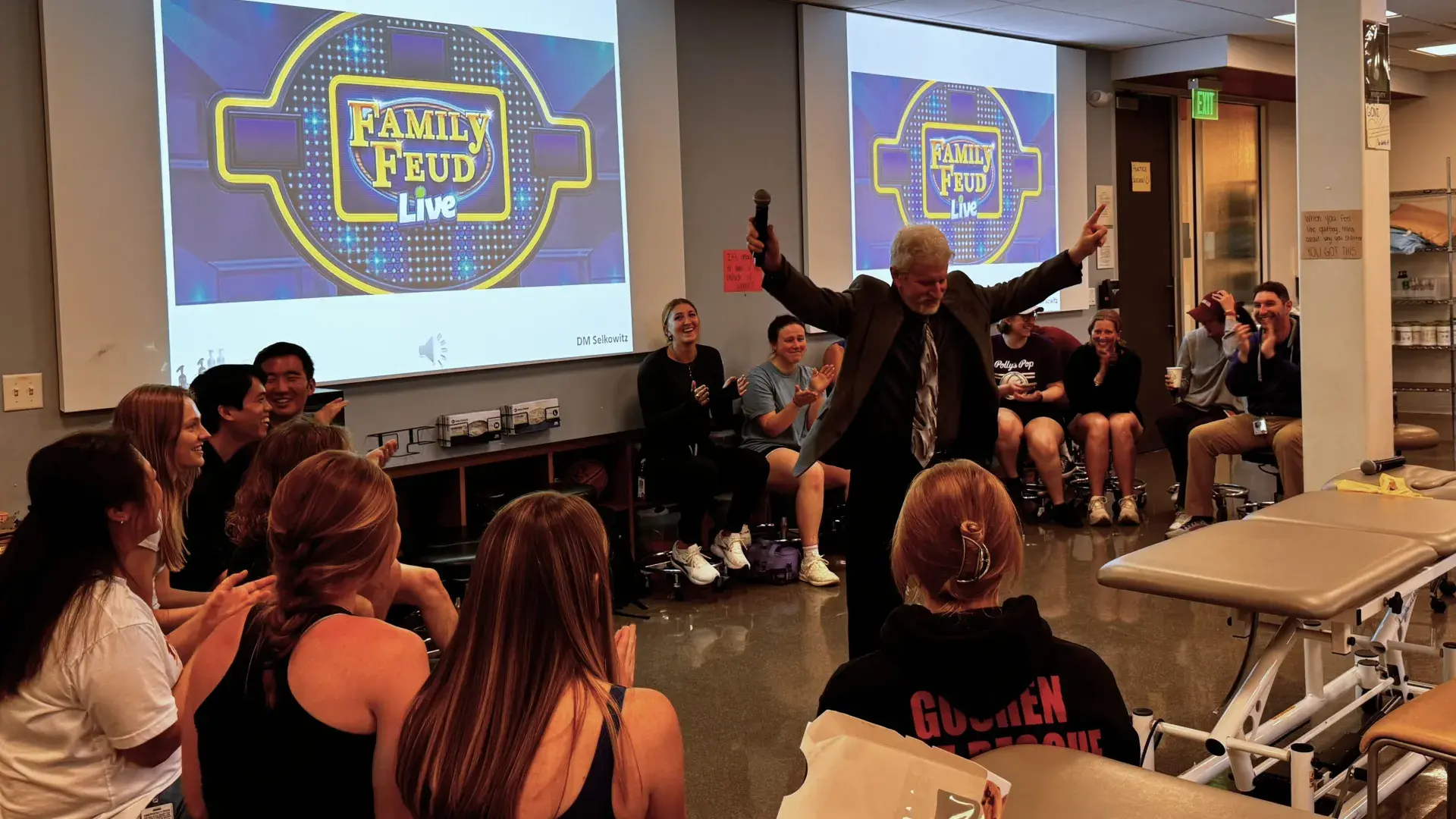 Professor with arms raised in front of family feud screens