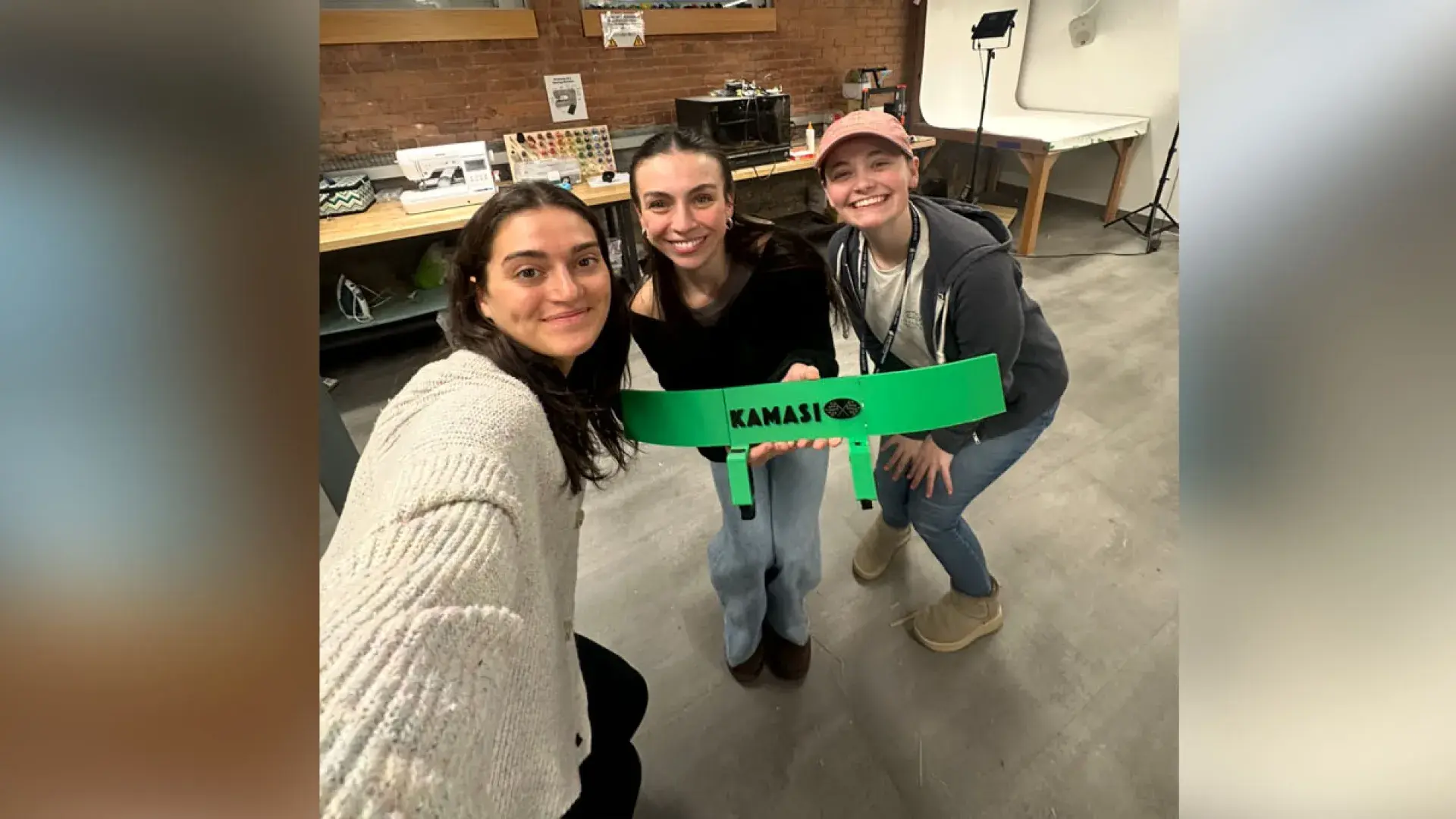 Three women pose holding up a green device