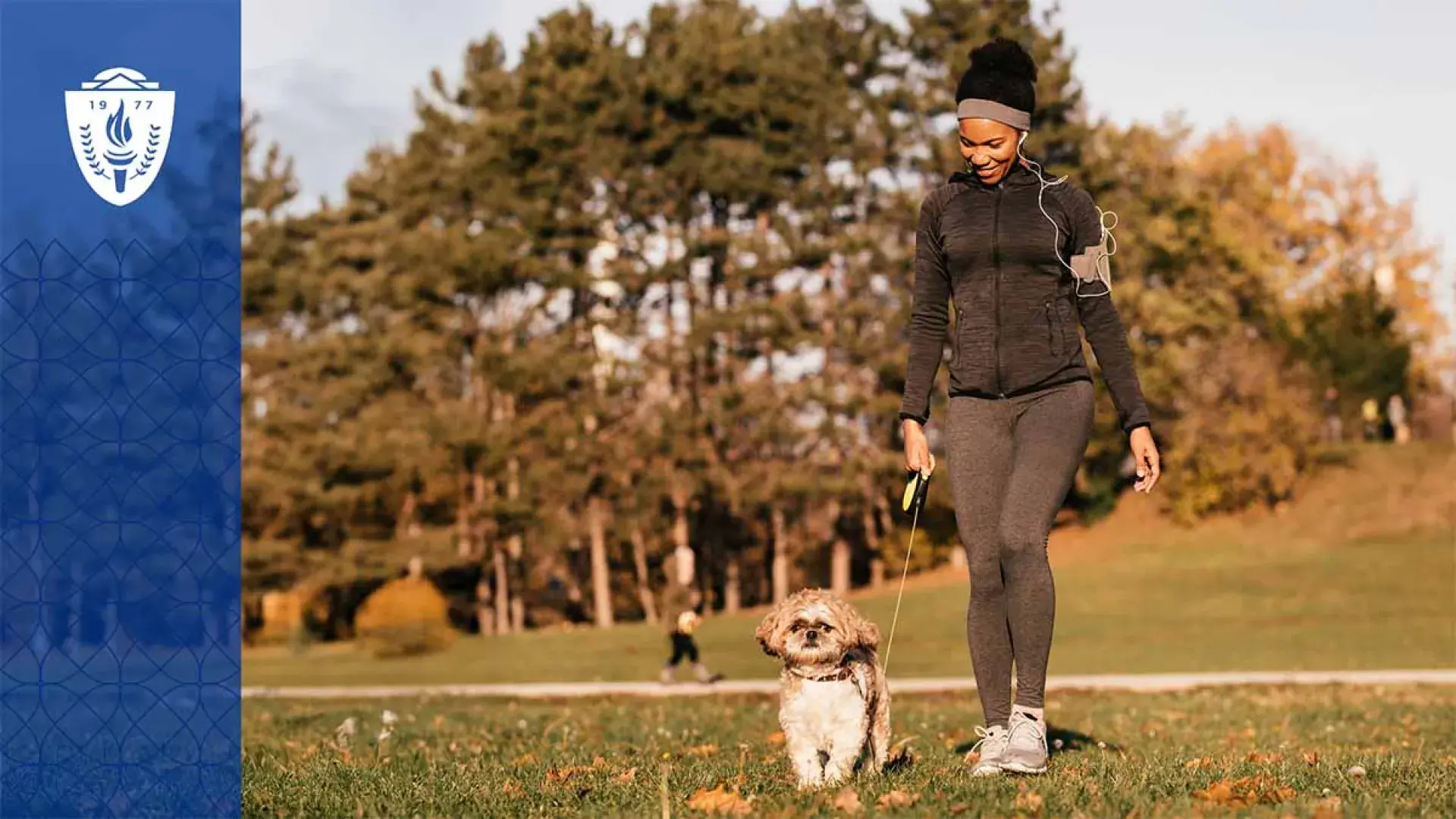Woman wearing a black jacket and walking a dog on a leash in a park