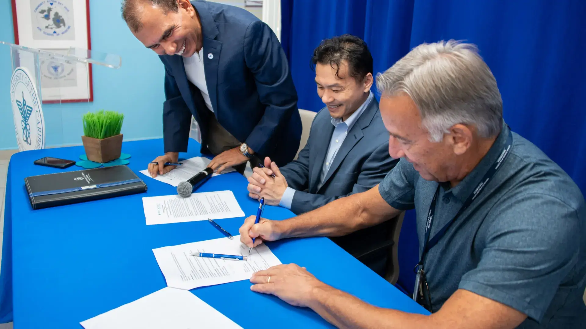 three men at a blue table signing some papers