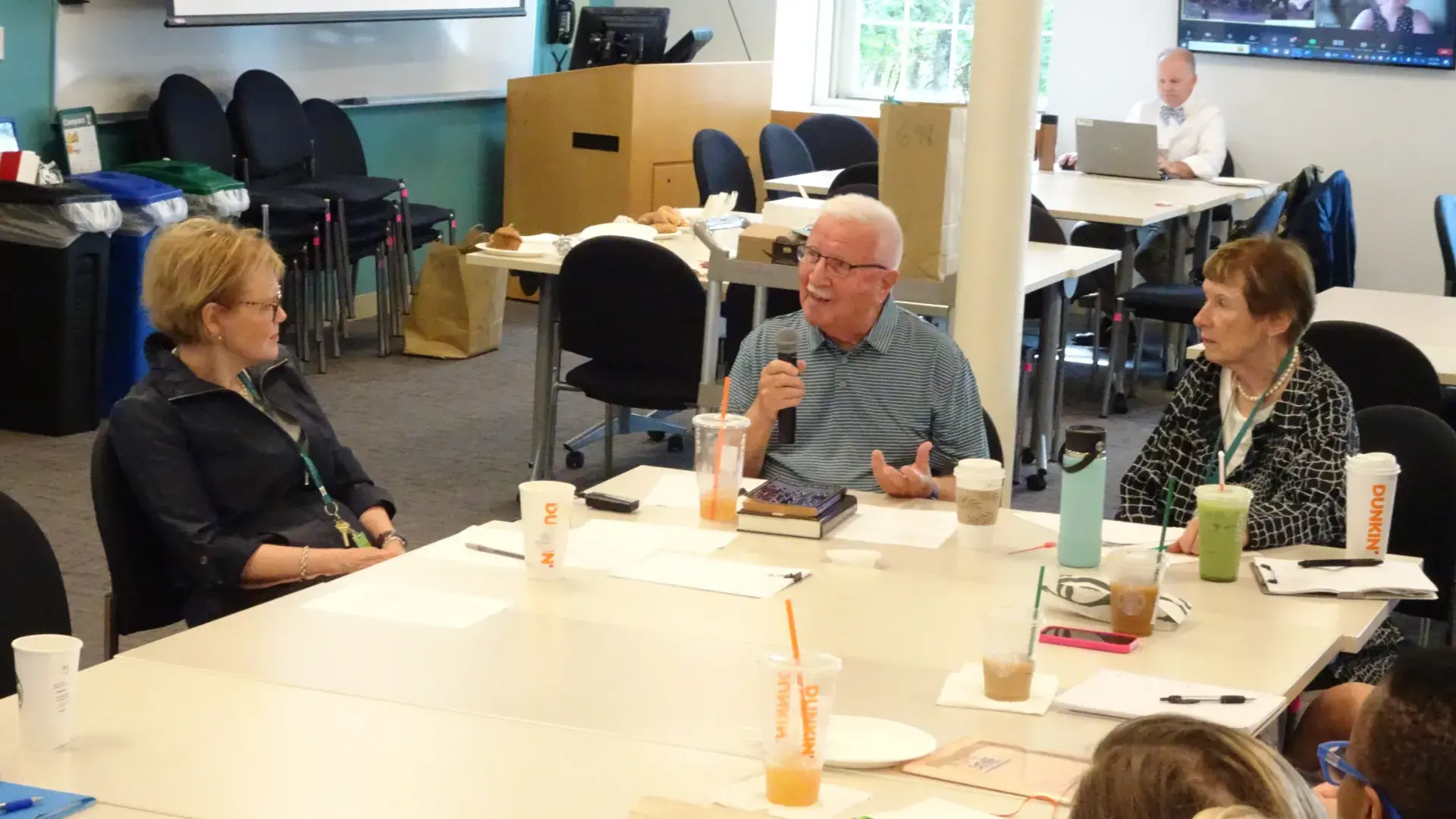 People sit around a table in a classroom and one holds a microphone