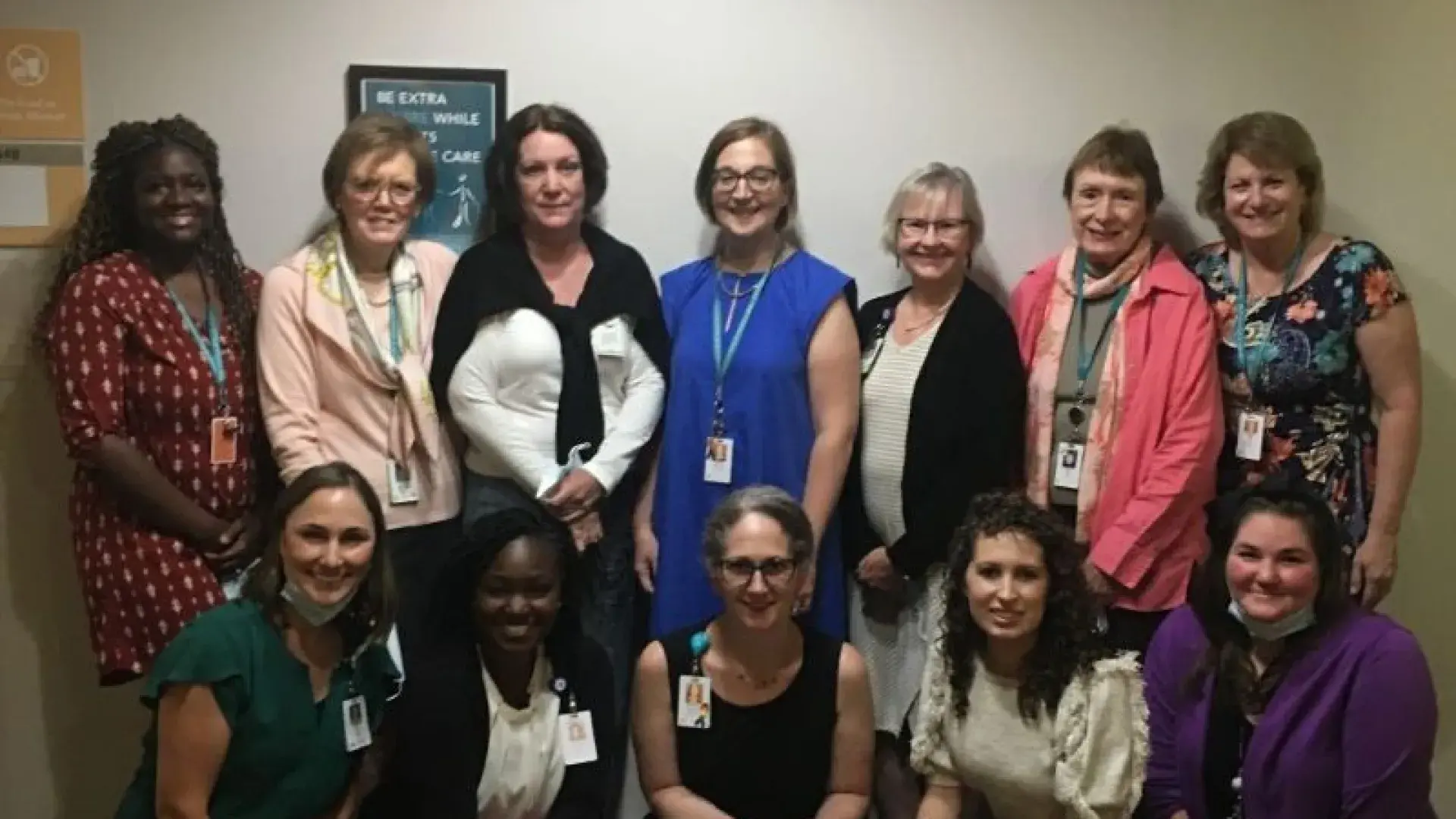 Five women kneel in front of seven other women to pose for a photo