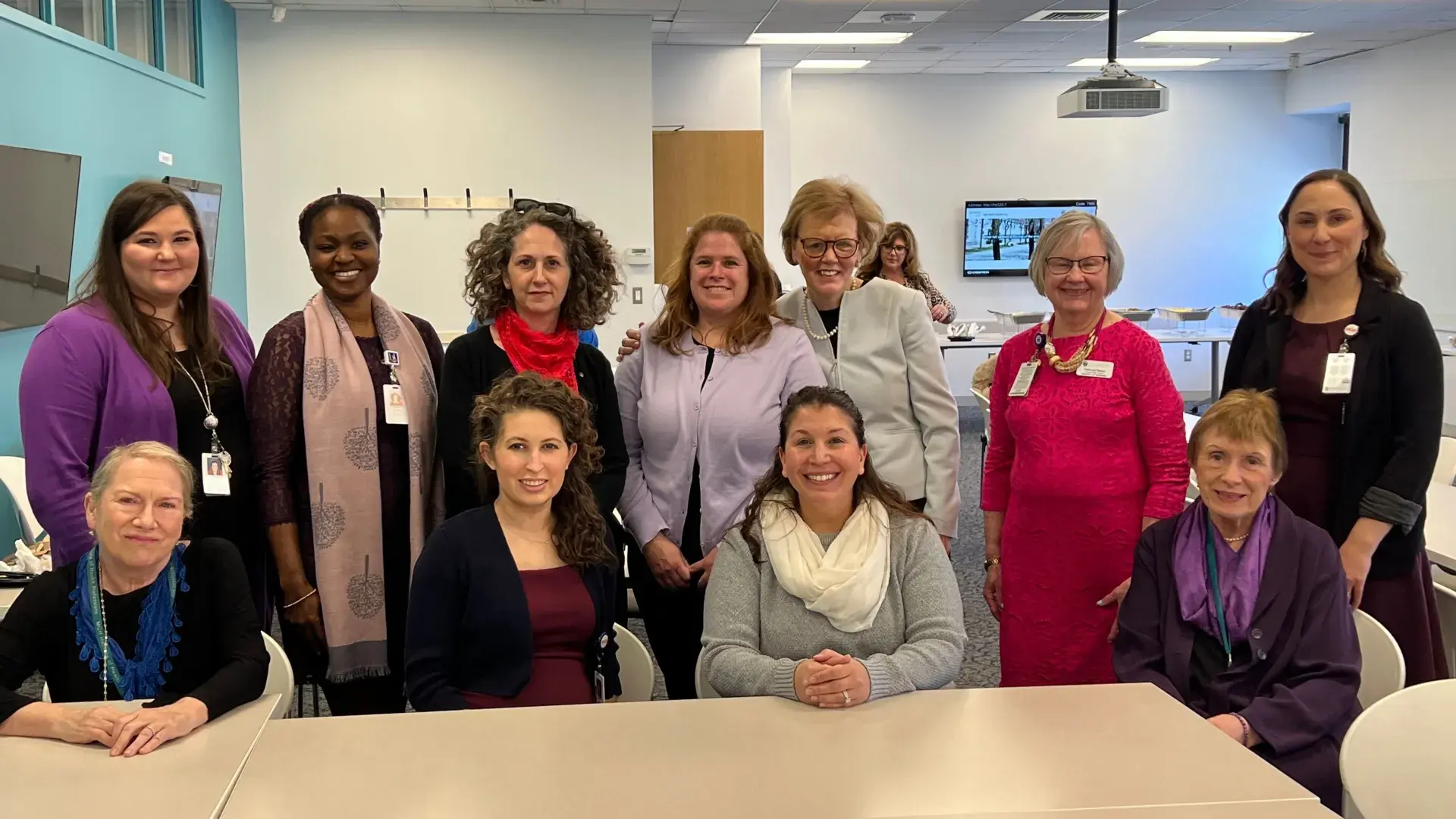 Eleven people stand or site at a table