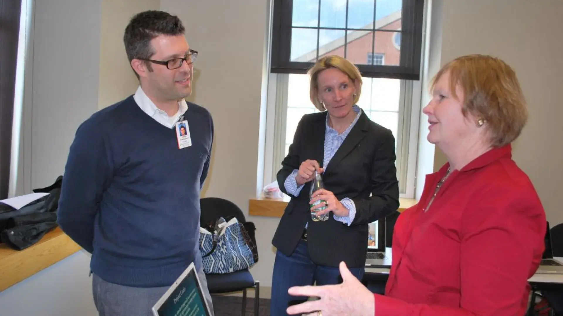 A woman stands in front of a laptop talking to two other people