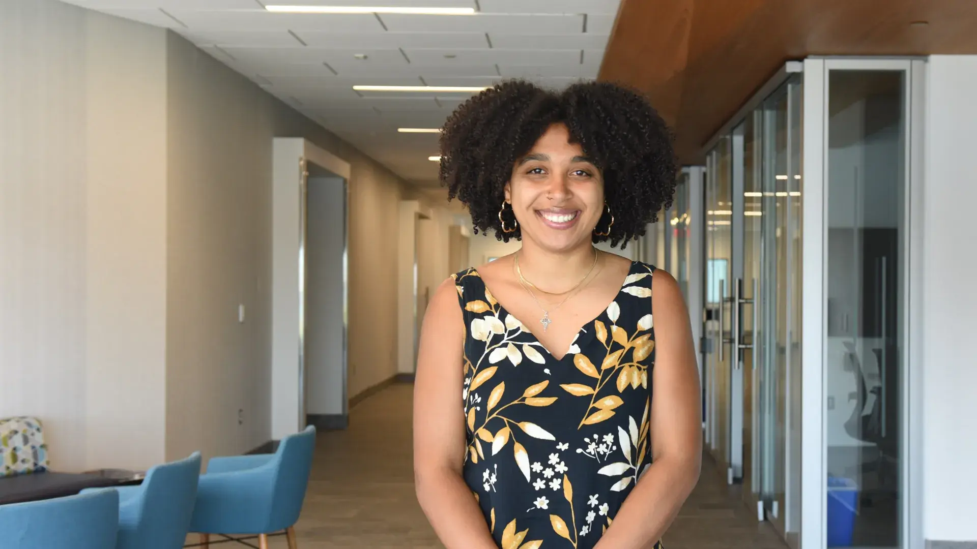 A woman stands with chairs to her right and glass rooms to her left