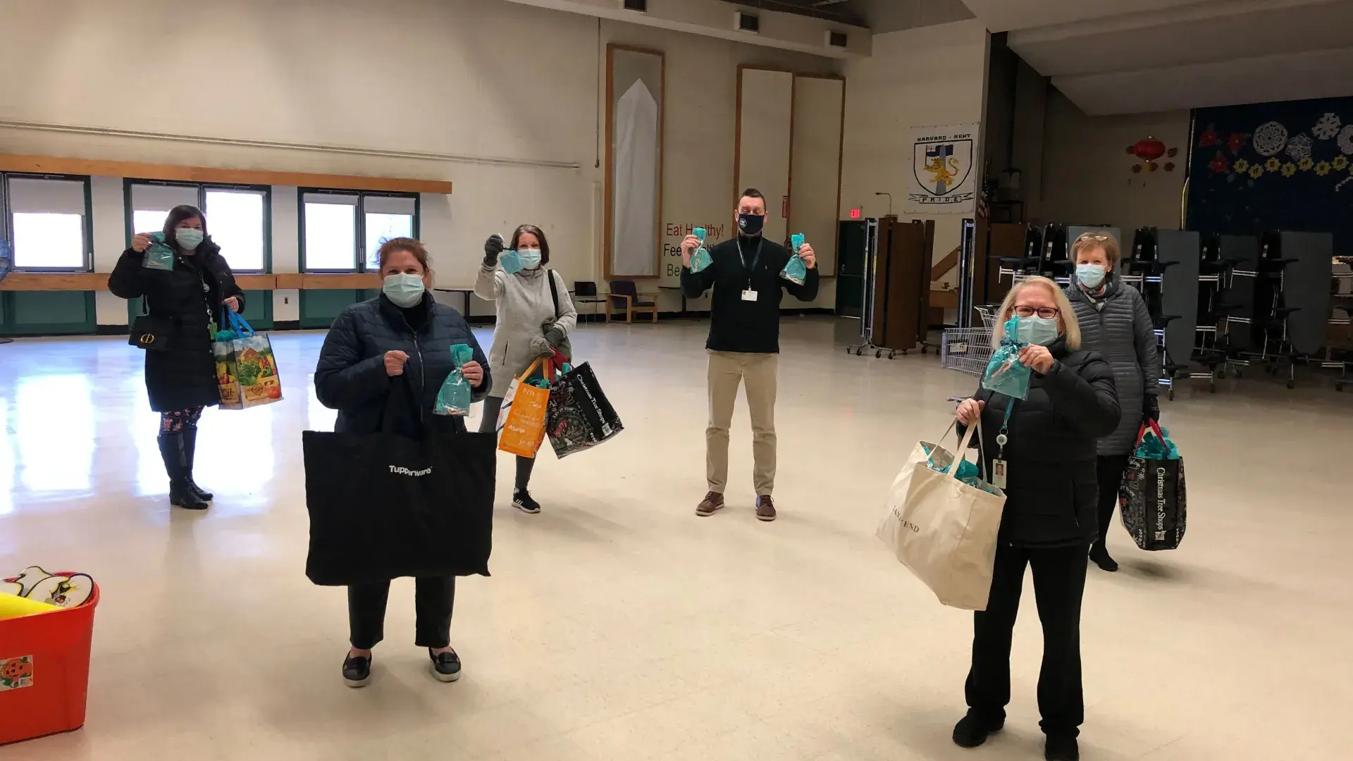 People wearing masks stand several feet apart holding bags