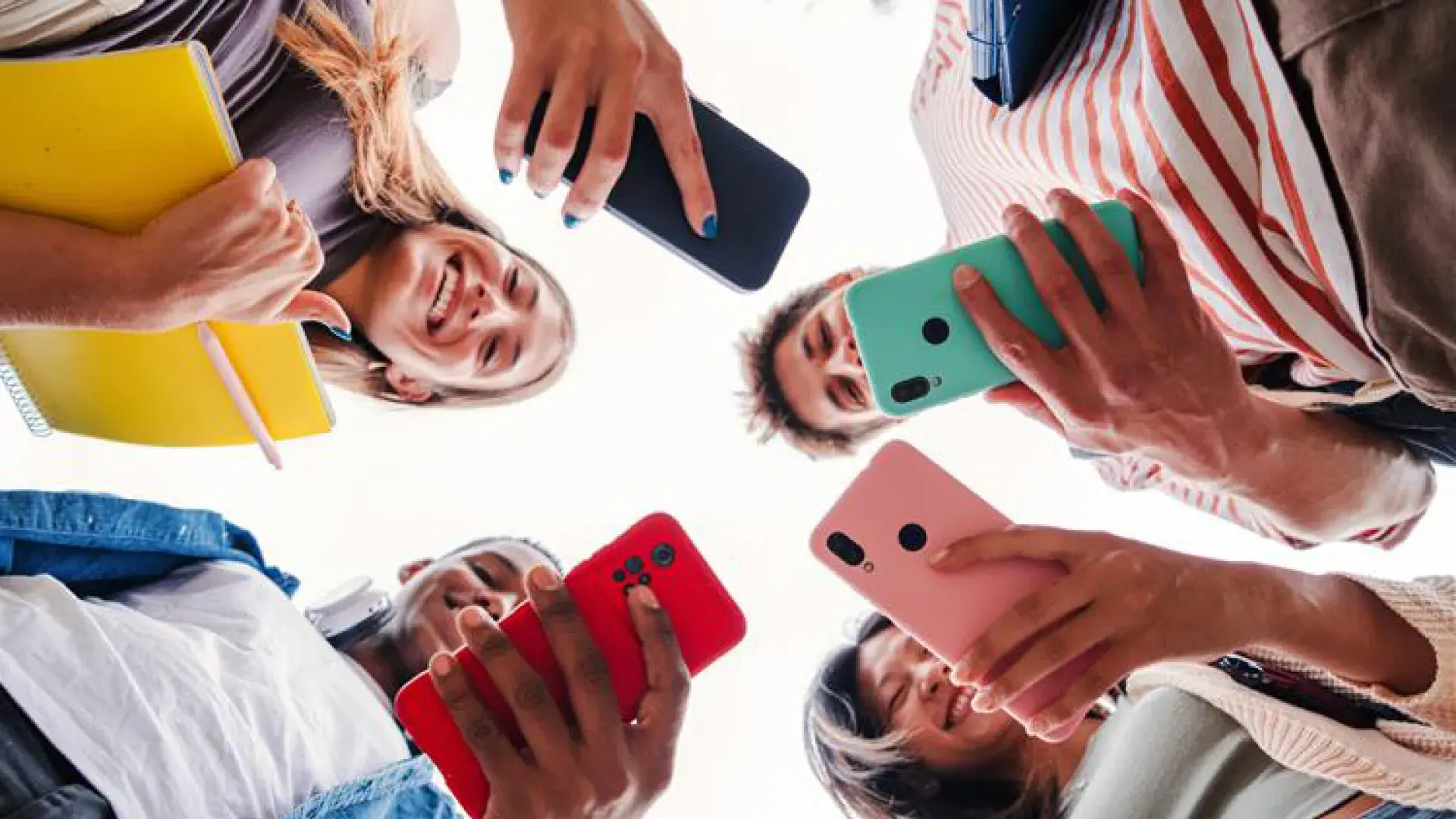 shot from below four college age people holding cell phones and folders in a circle