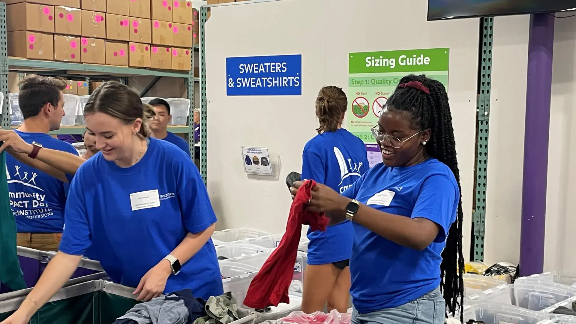 women and men in matching blue t shirts printed with "community impact" sort clothes into bins