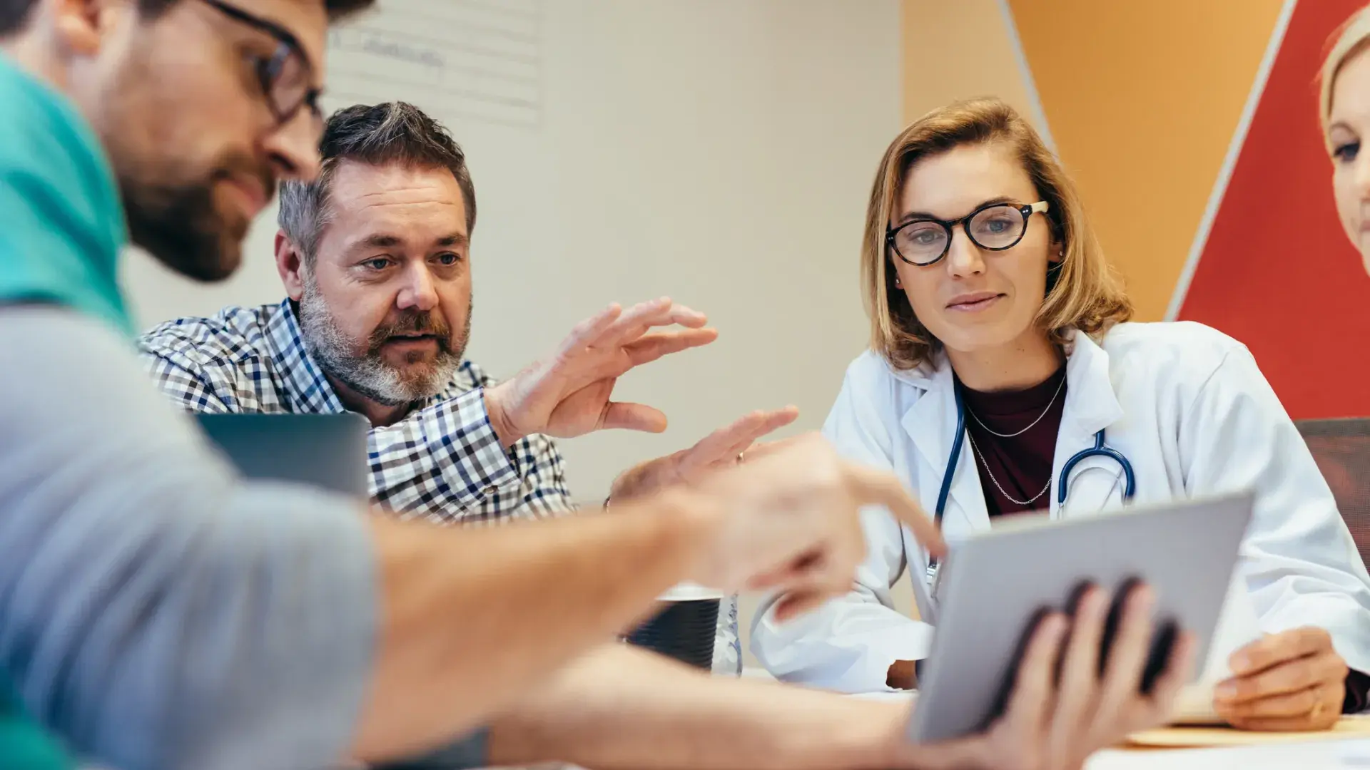 meeting where a bearded man in a business shirt points out something on an ipad to a woman in a lab coat