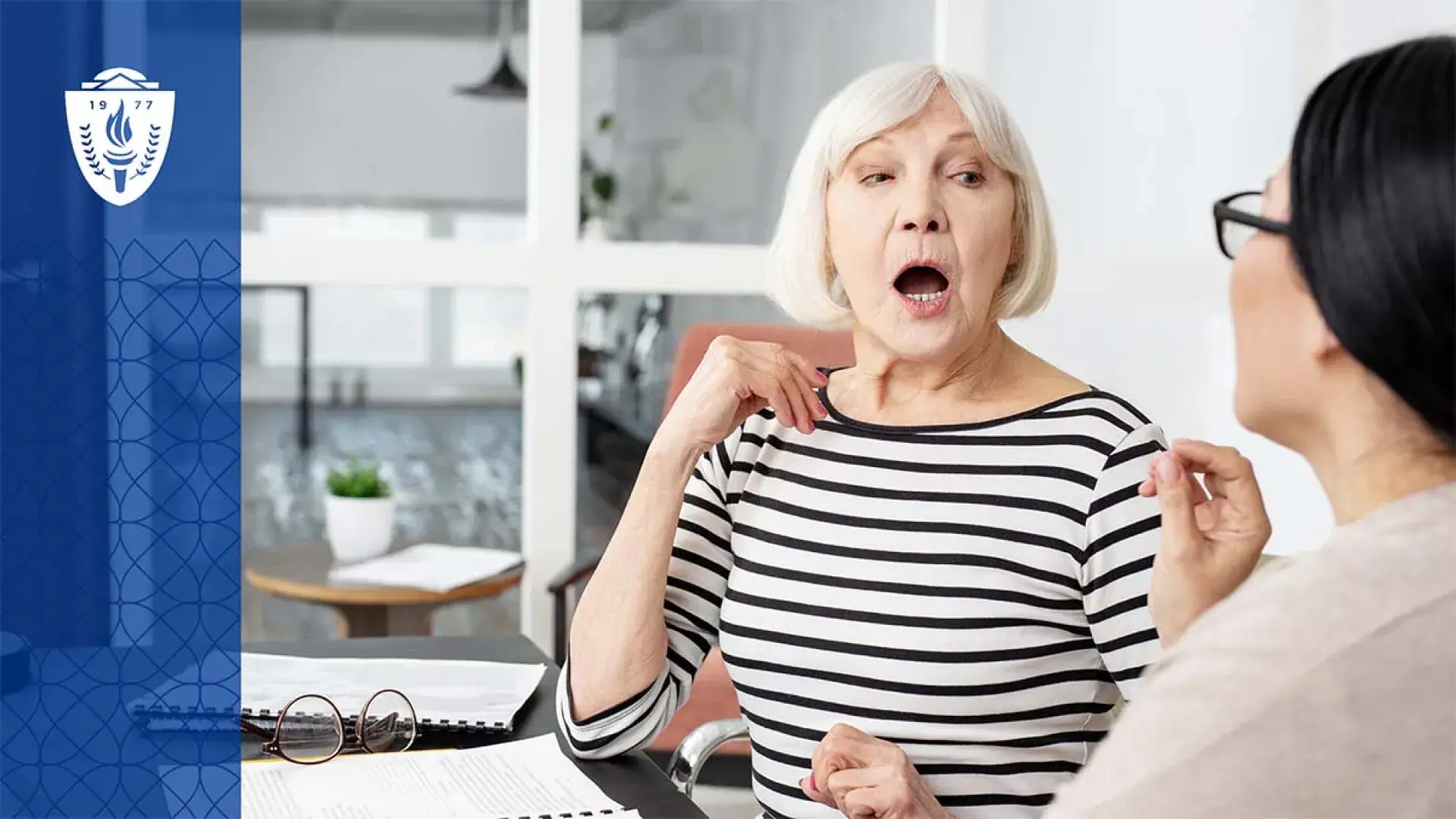 Older woman with white hair sitting at a table working with a speech language pathologist