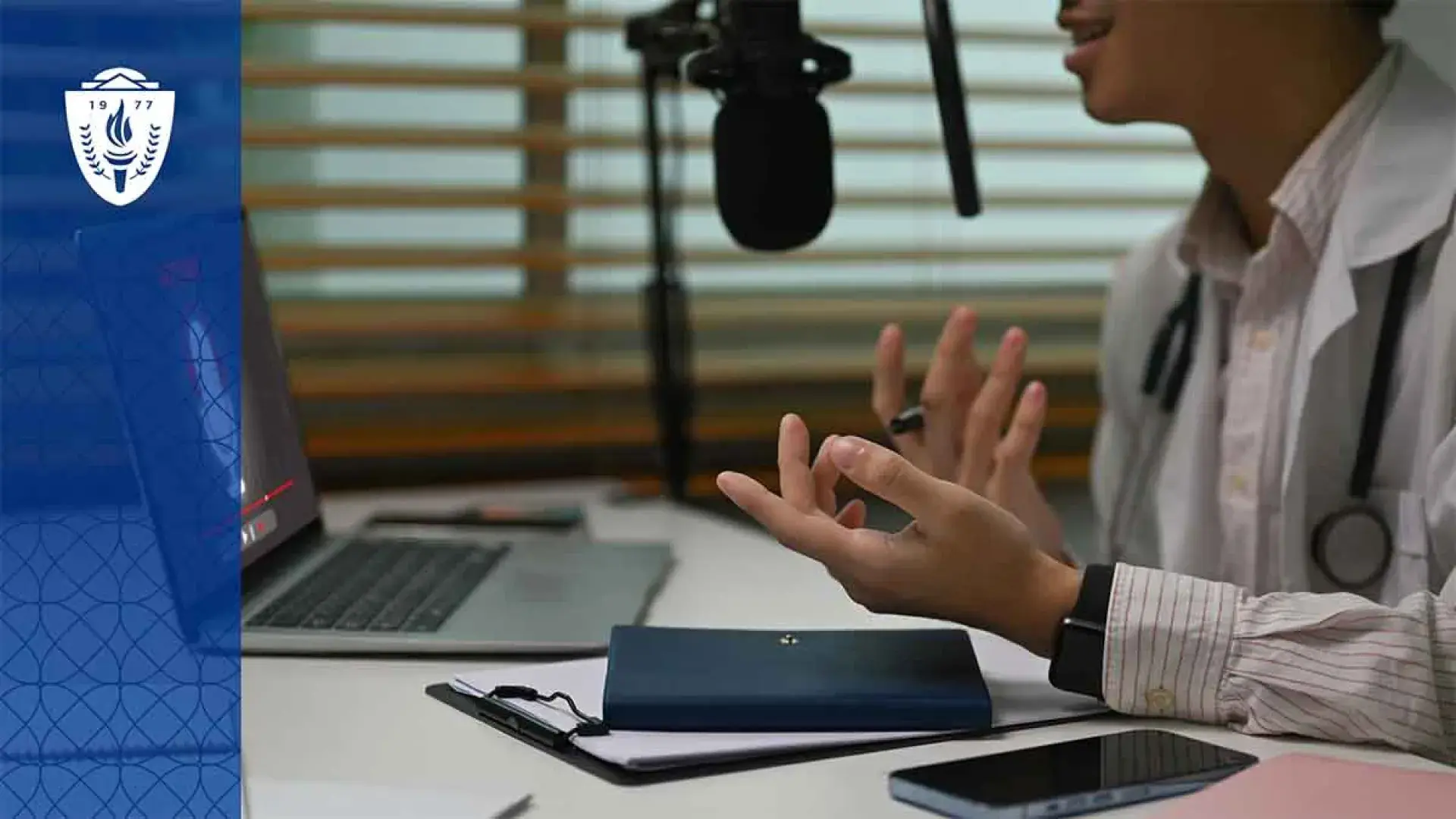 Doctor sitting at desk in front of a laptop and talking into a microphone