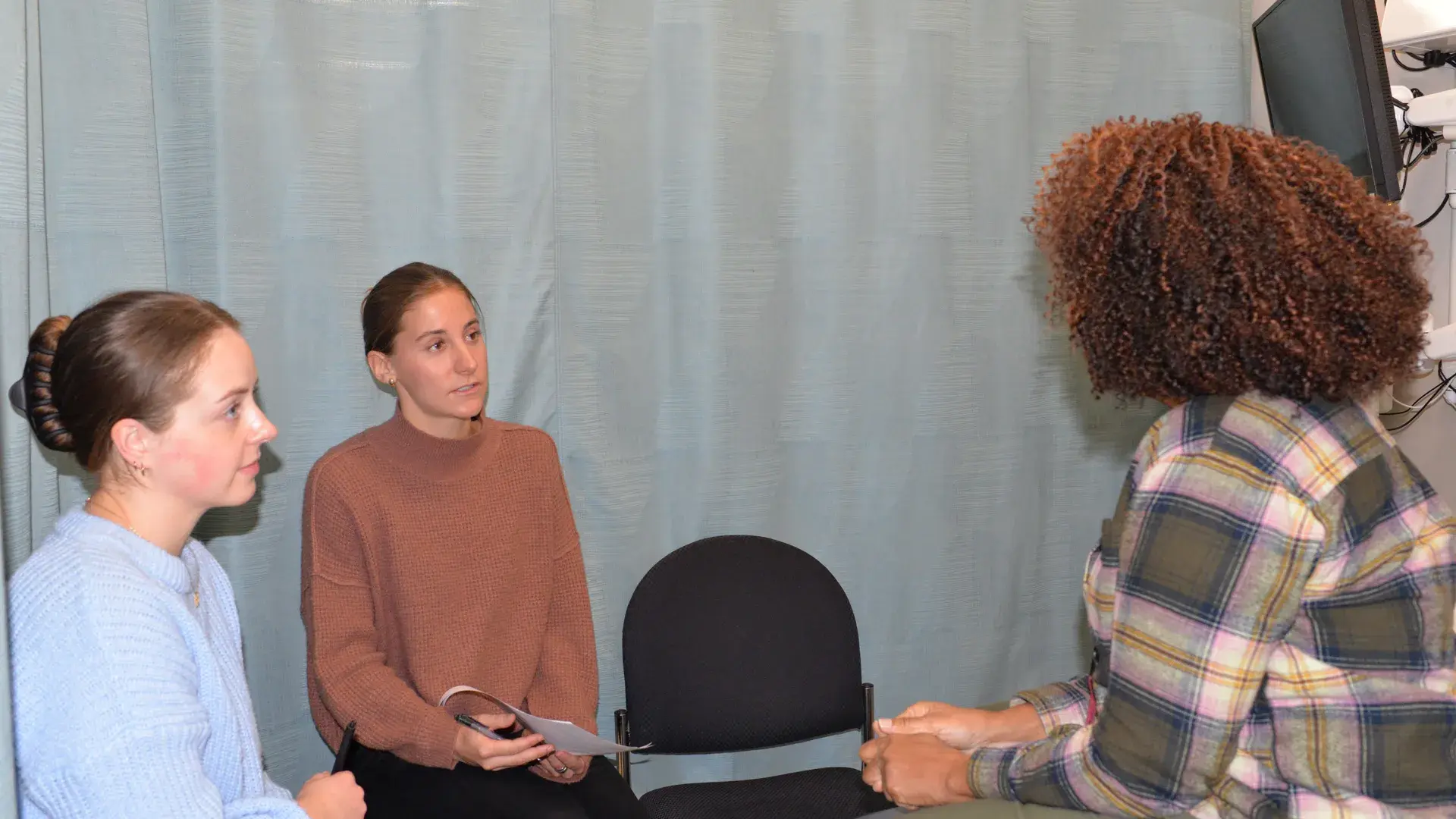 3 women speaking in front of a blue hospital curtain