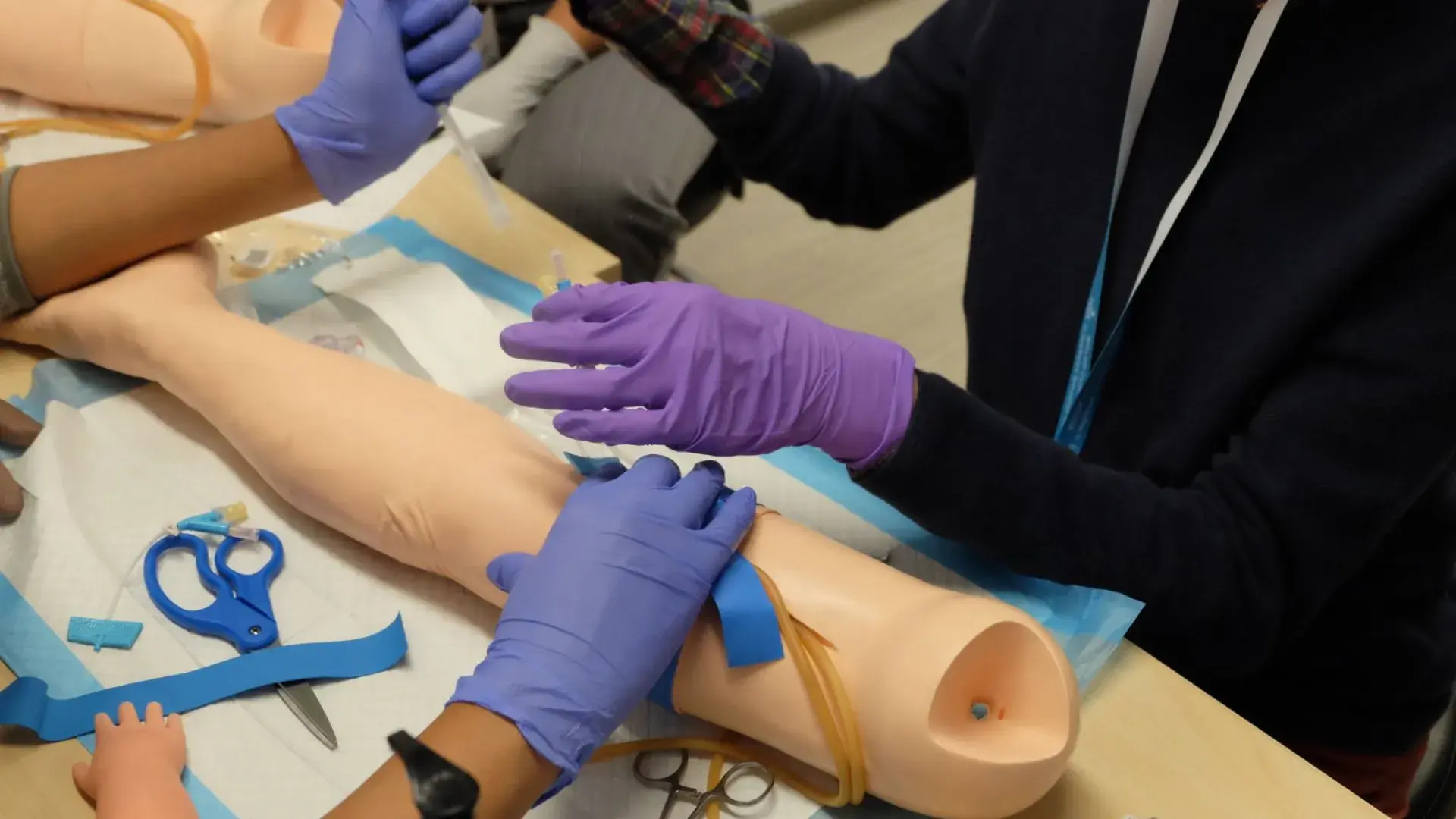 People wearing glove work on a manikin's are with medical equipment
