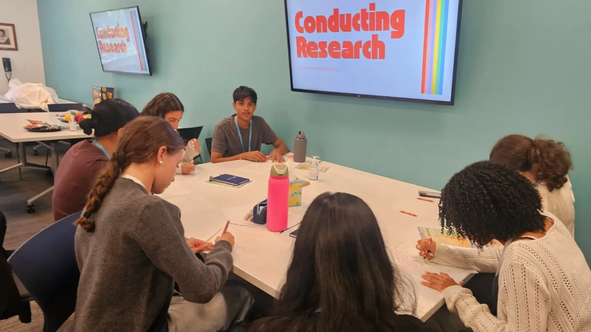People sit around a table under a screen that says conducting research