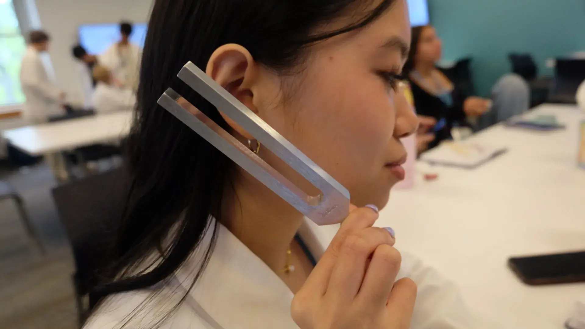 A woman holds a tuning fork next to their ear